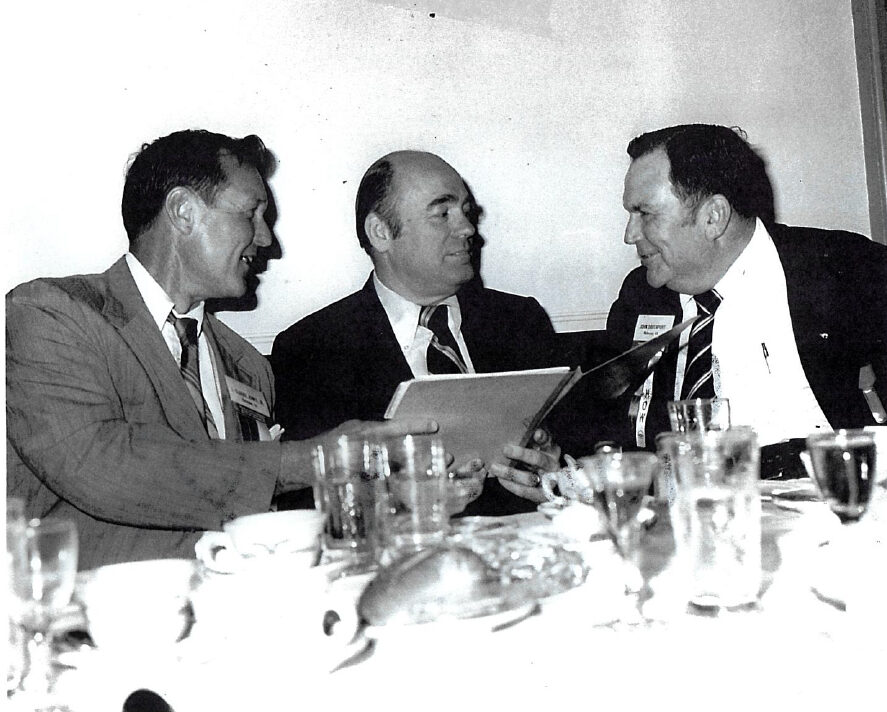 Historical photograph showing industry professionals in a formal discussion setting.