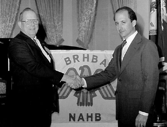 Historical photograph of an HBAV leader shaking hands in front of a BRHBA and NAHB banner.