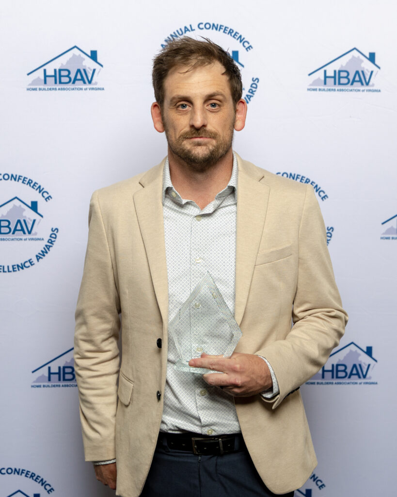 Man in a beige blazer and patterned shirt holding a clear acrylic award plaque.