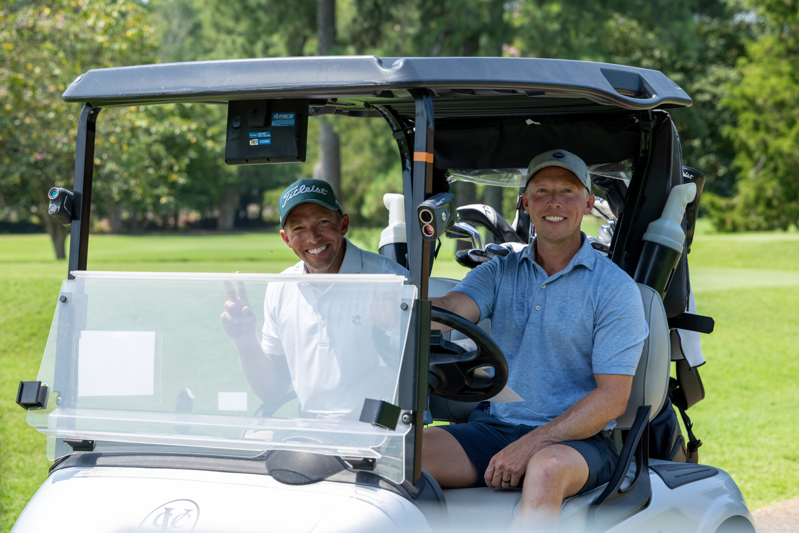 Two men smiling and posing for a photo inside a golf cart.