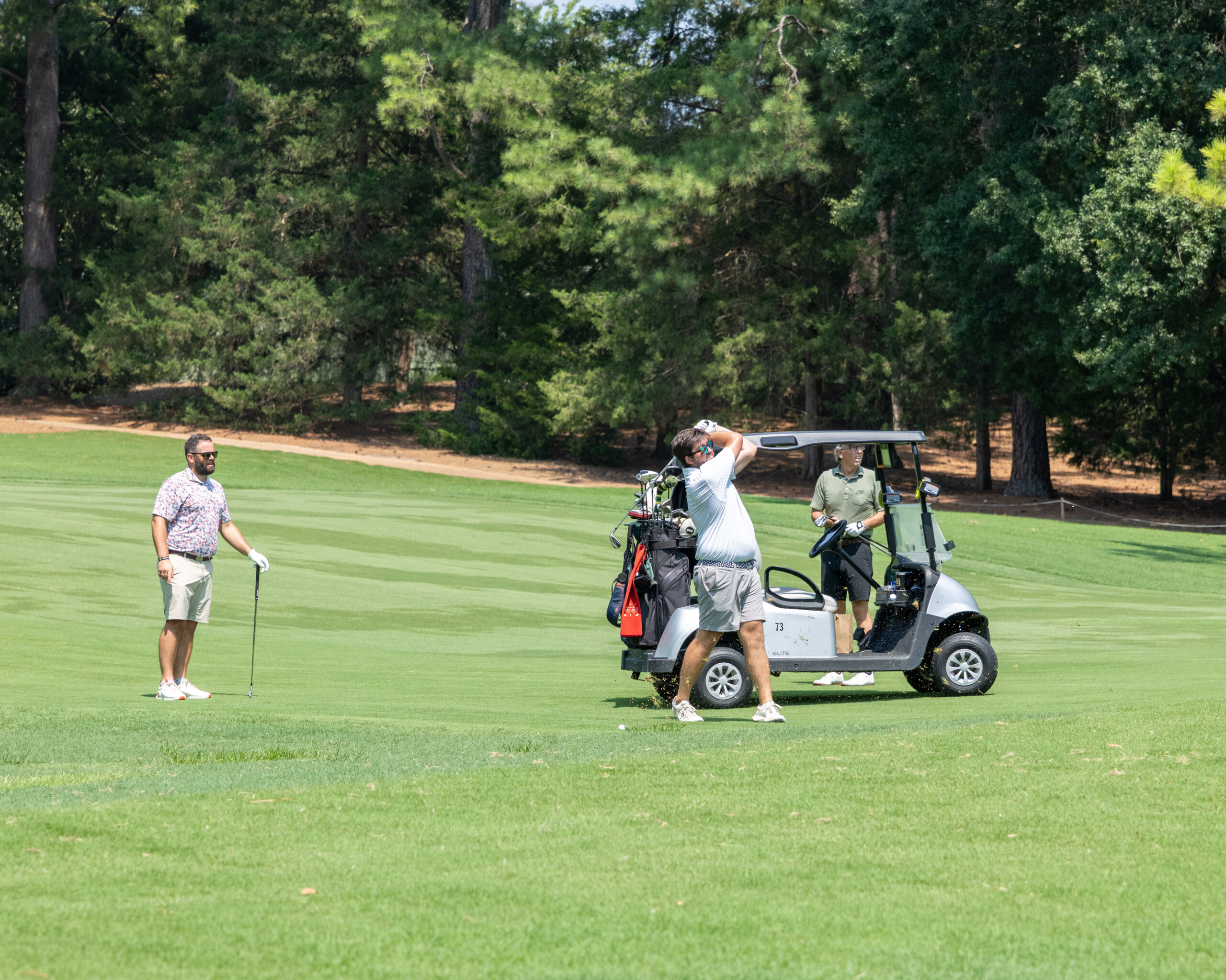 Two men and one woman on a golf course during a tournament.