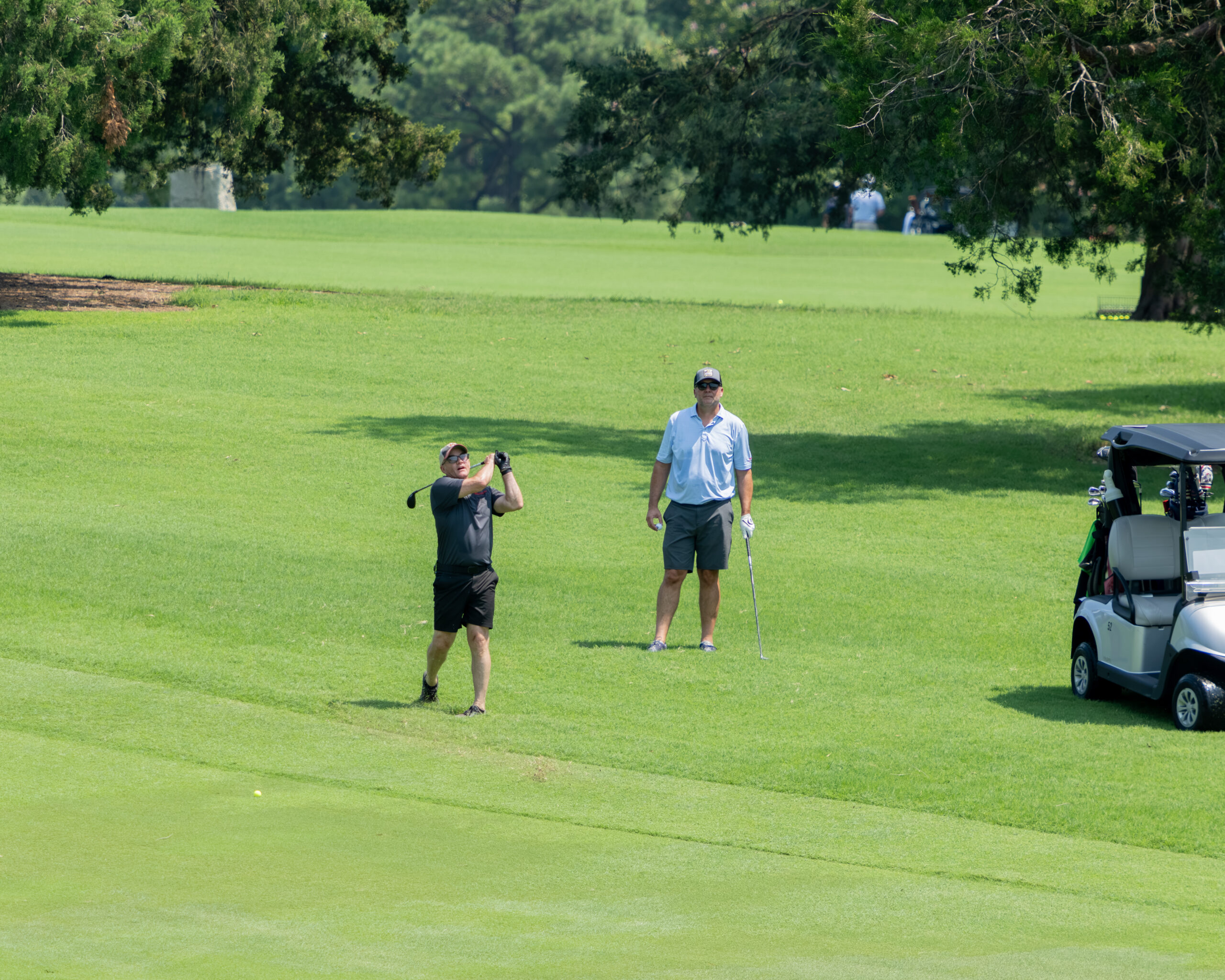 Two golfers stand on a green with a golf cart nearby.
