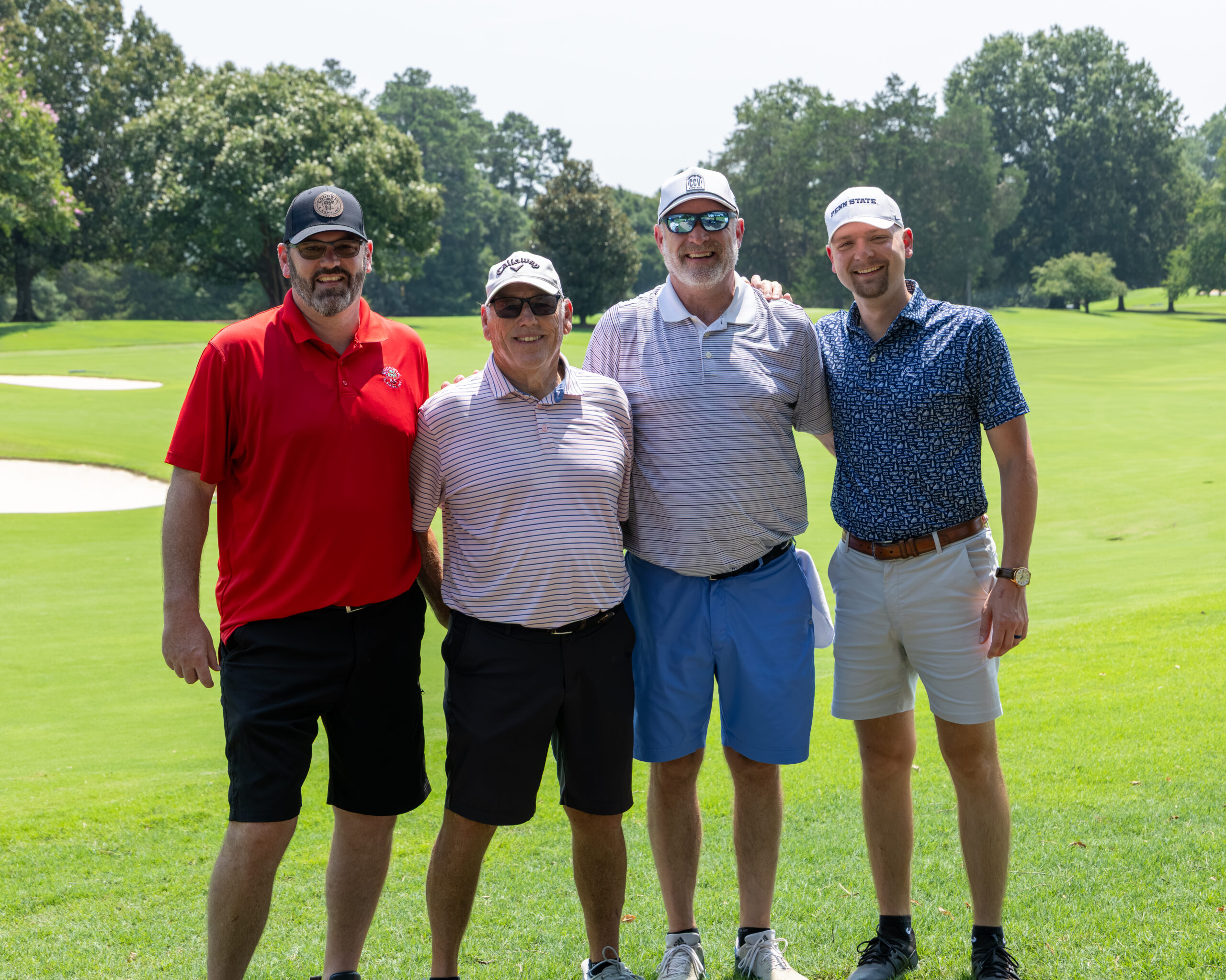 Four men in golf attire stand on a green at a golf course.