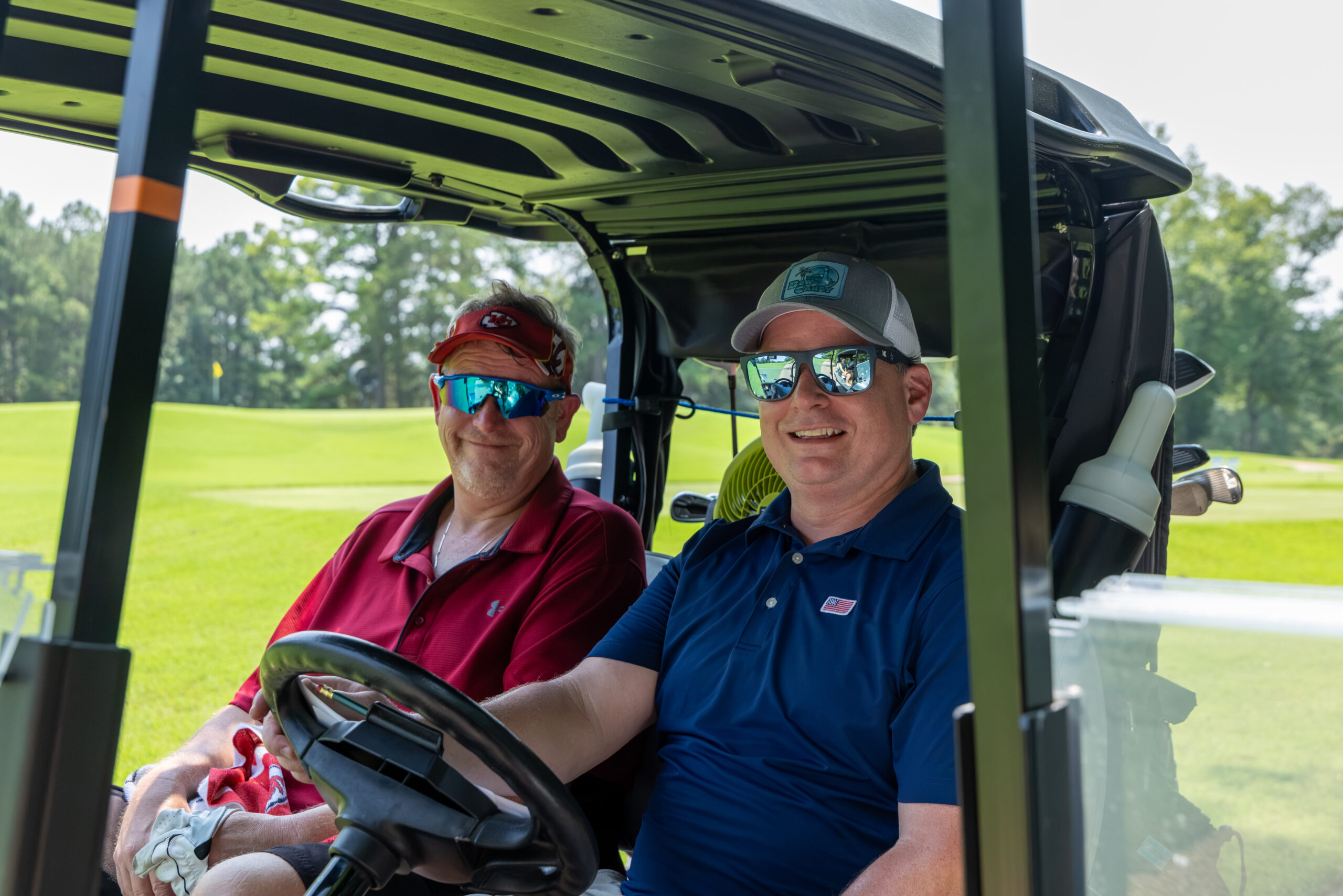 Two men smiling while riding in a golf cart on a course.