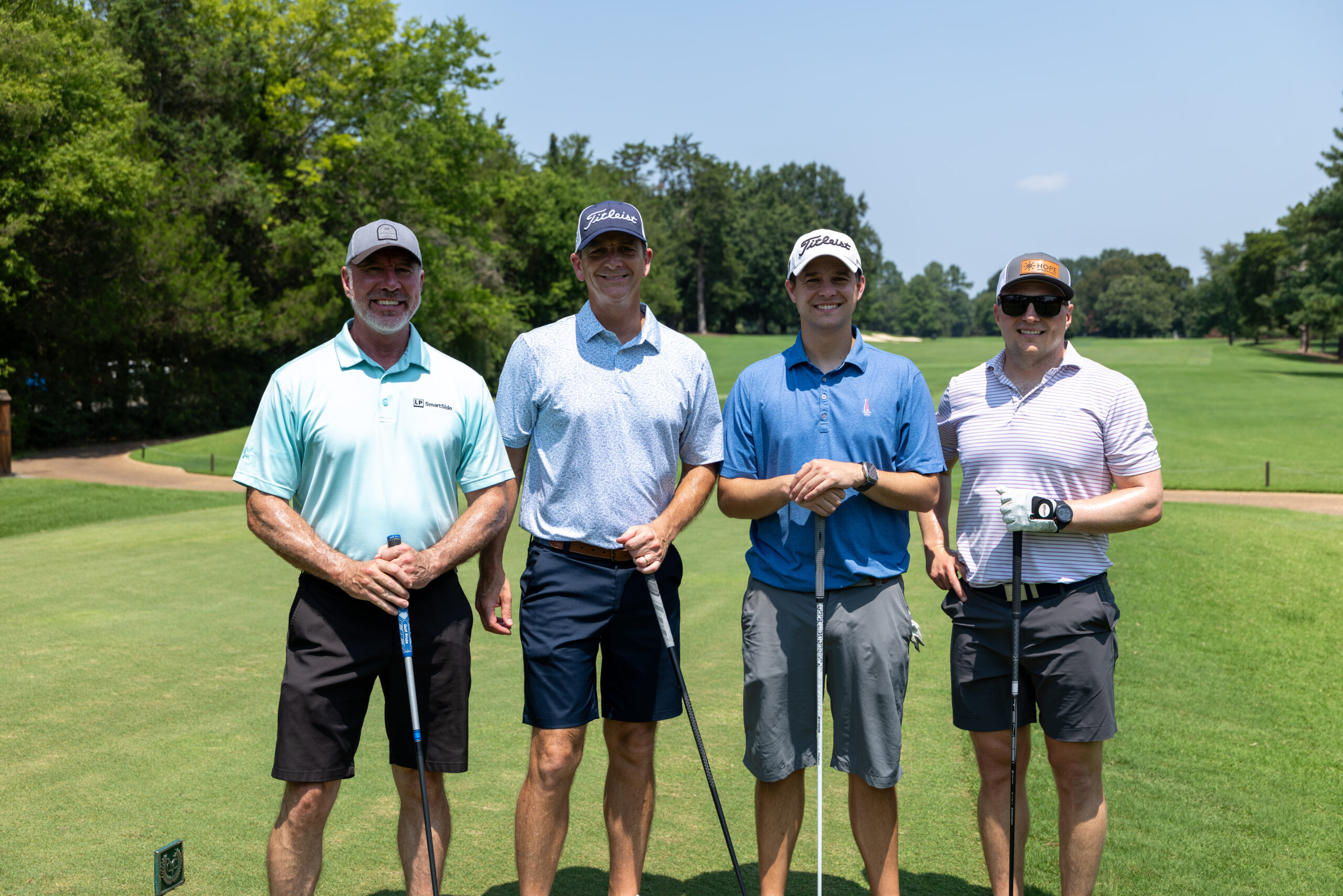 Four men in golf attire standing on a green at a golf course.