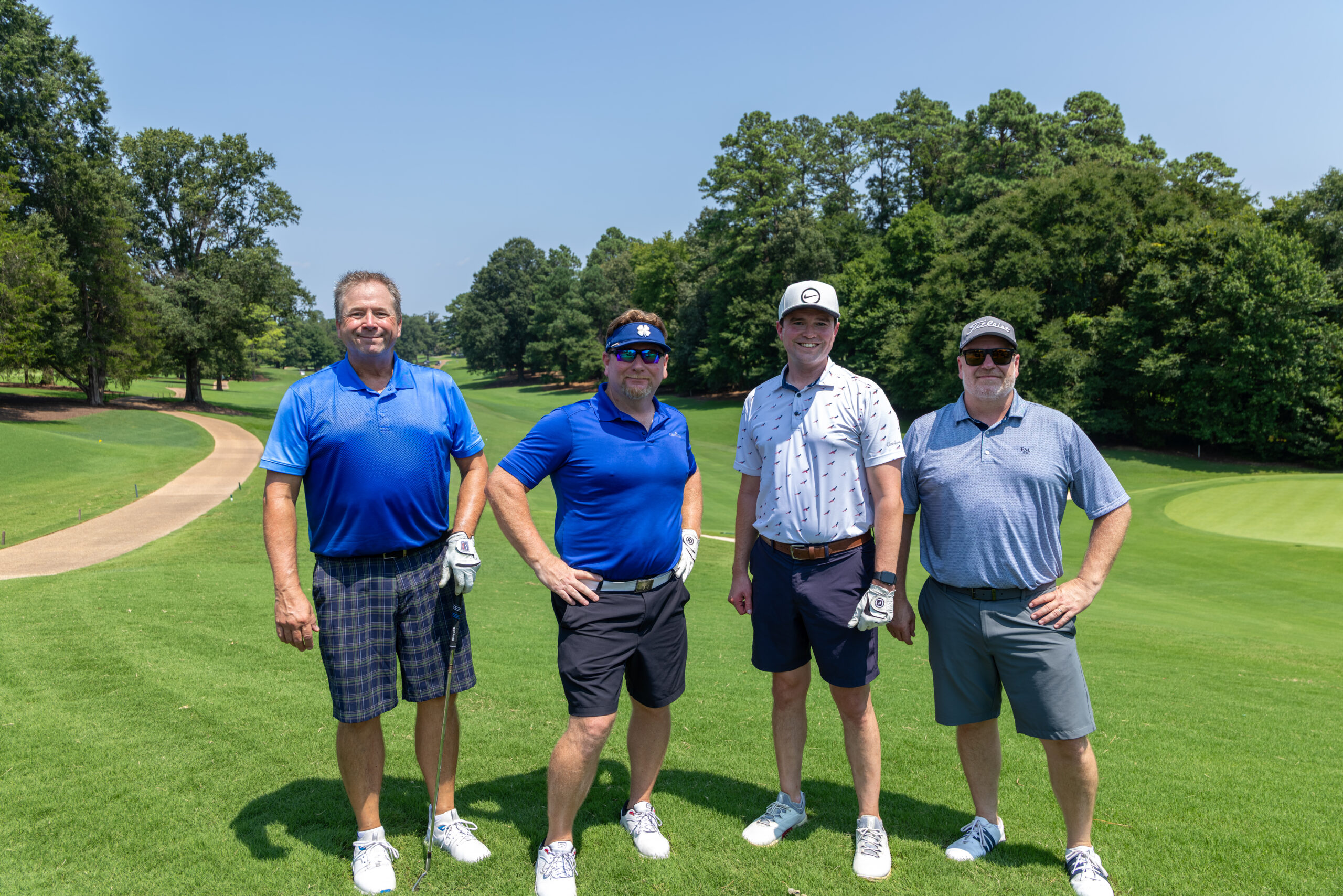 Four men in golf attire standing together on a green at a golf course.