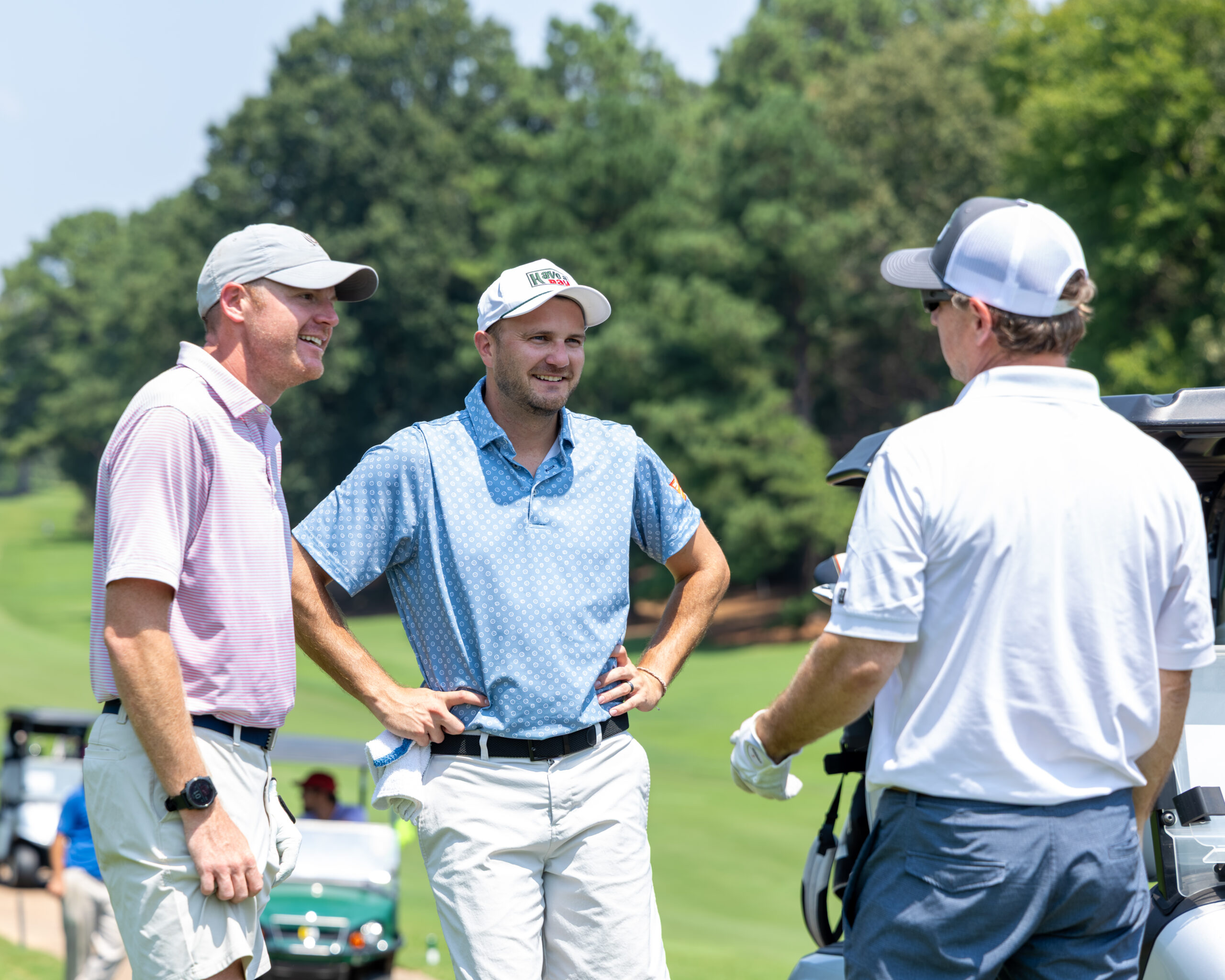Three men in golf attire standing on a golf course near a cart.