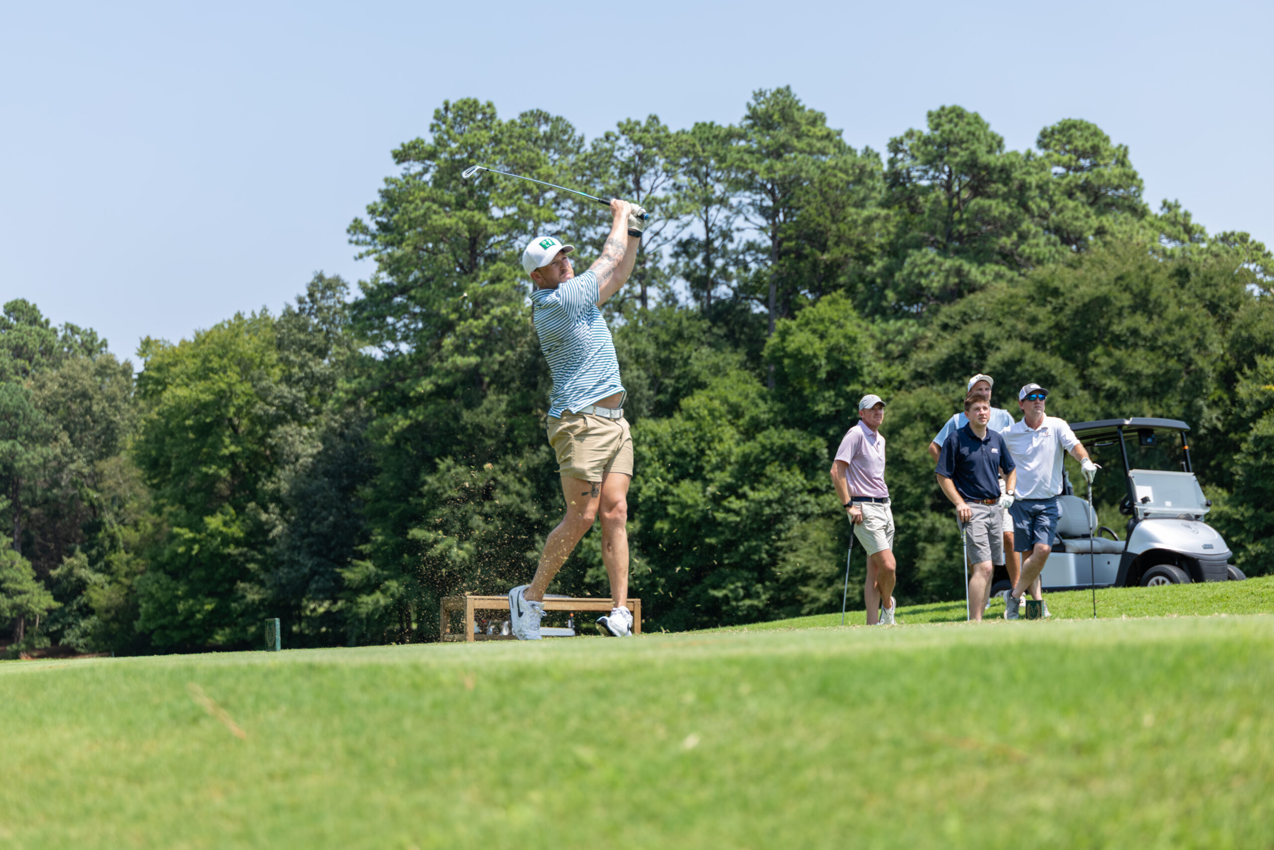 A man golfer follows through on his swing at a golf course with three other men standing nearby.
