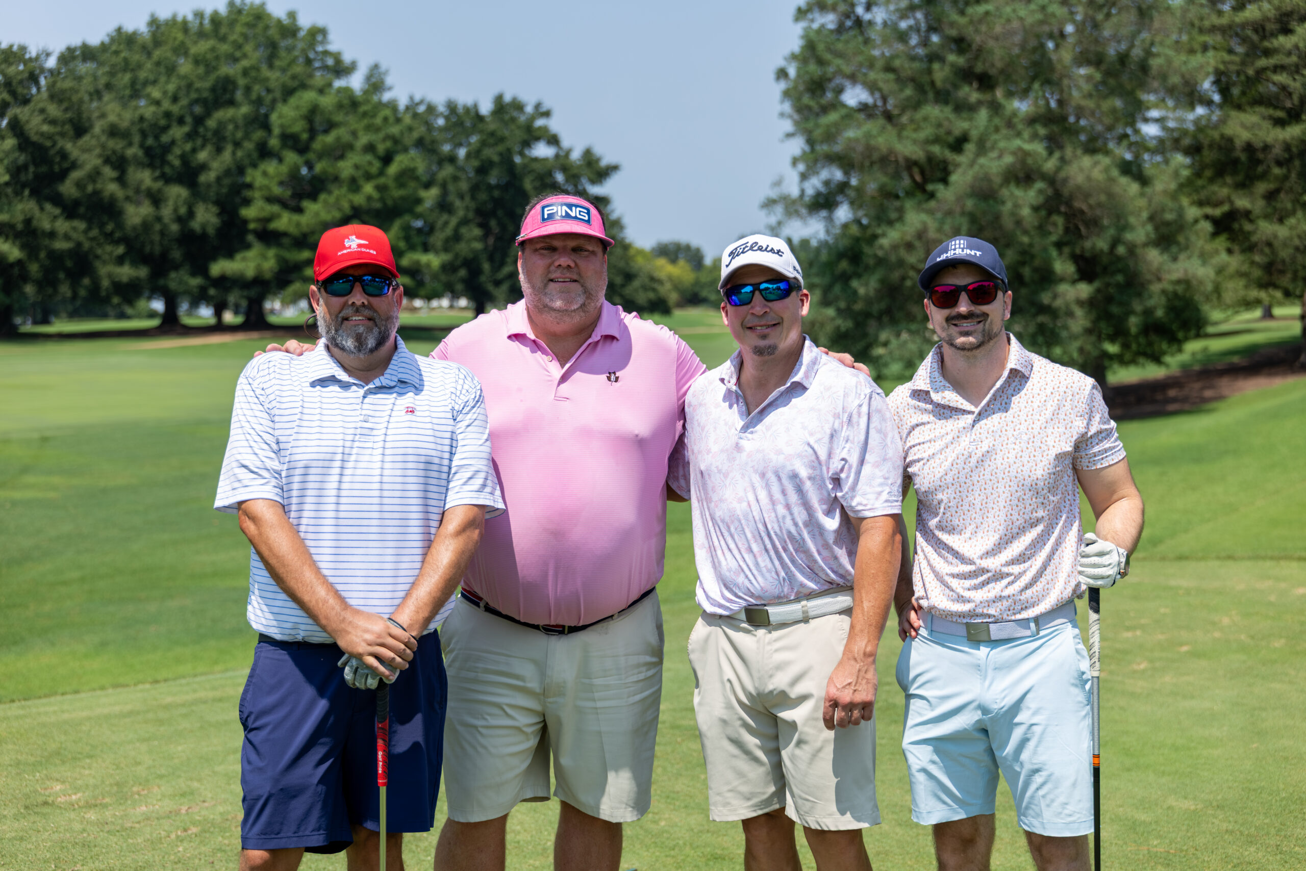 Four men standing together on a golf course, posing for a photo.