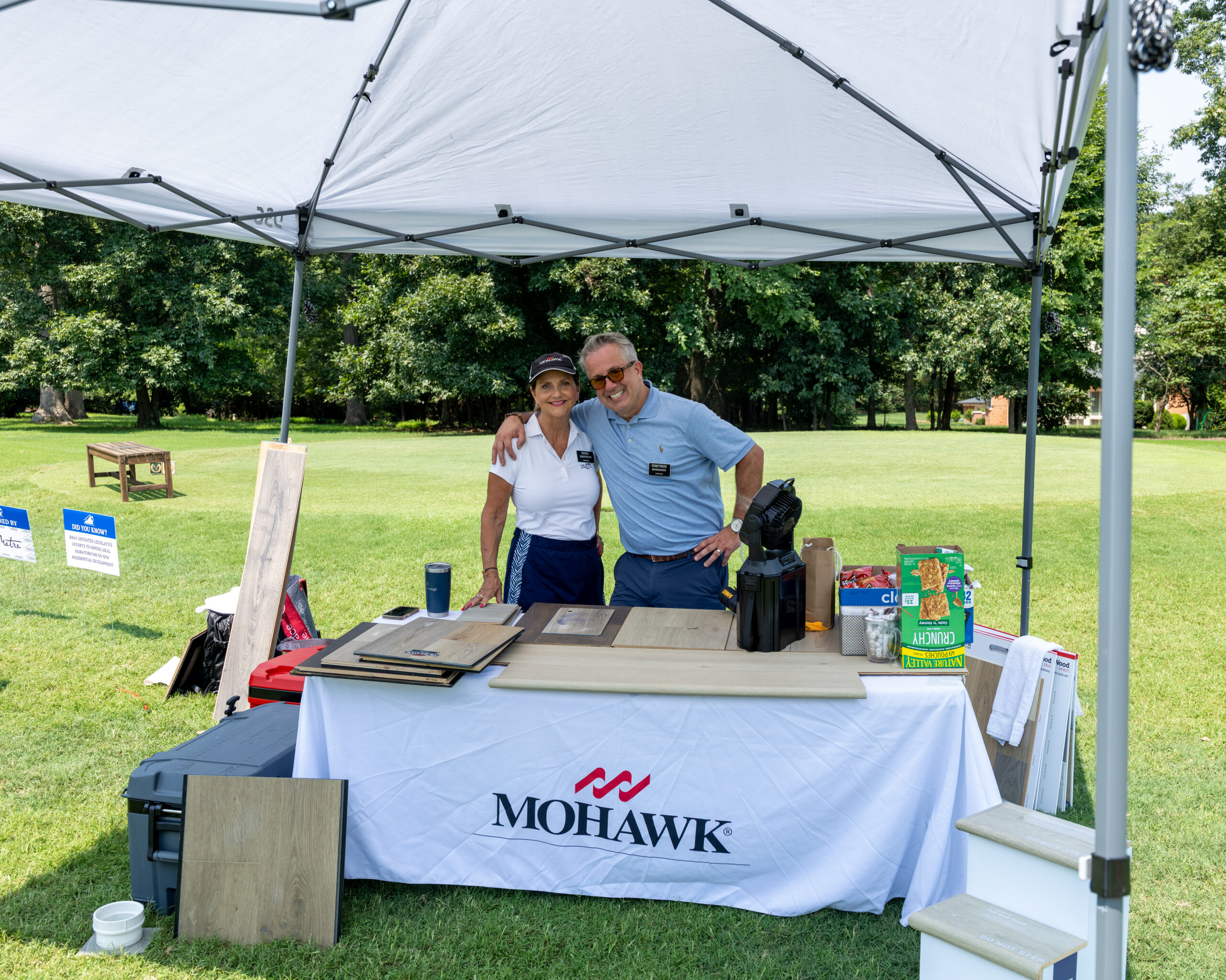 A man and woman stand behind a white table with products under a large canopy tent.