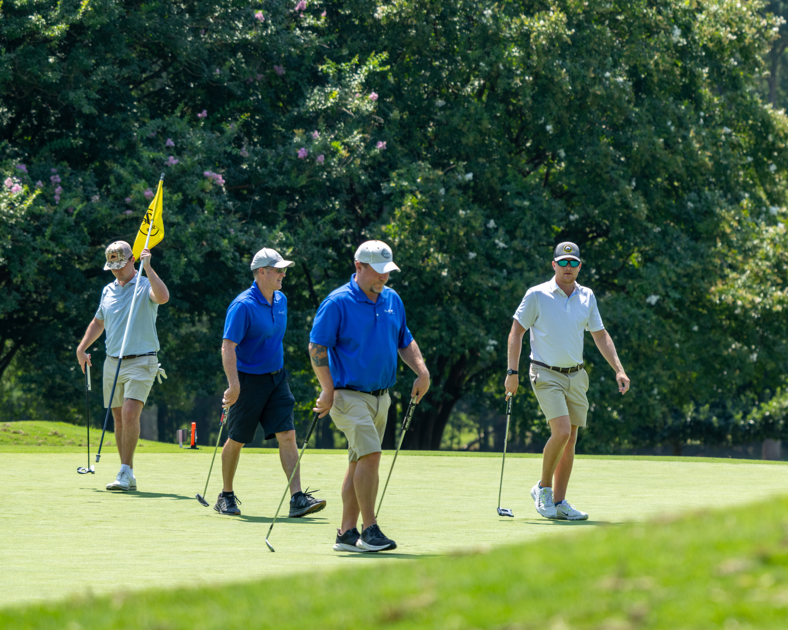 Four men on a golf green with clubs and a flag