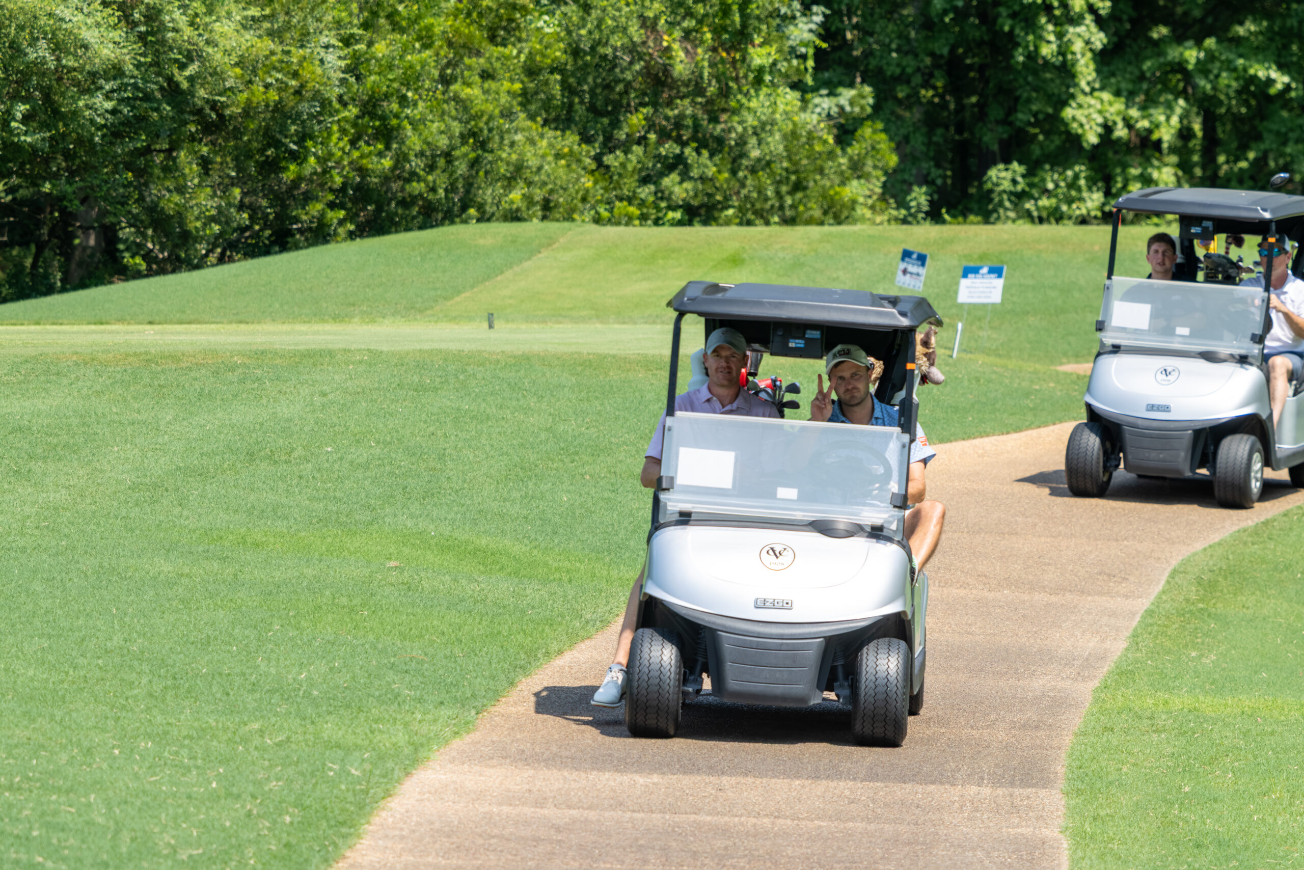 Two women on a golf cart on a path near a green fairway.