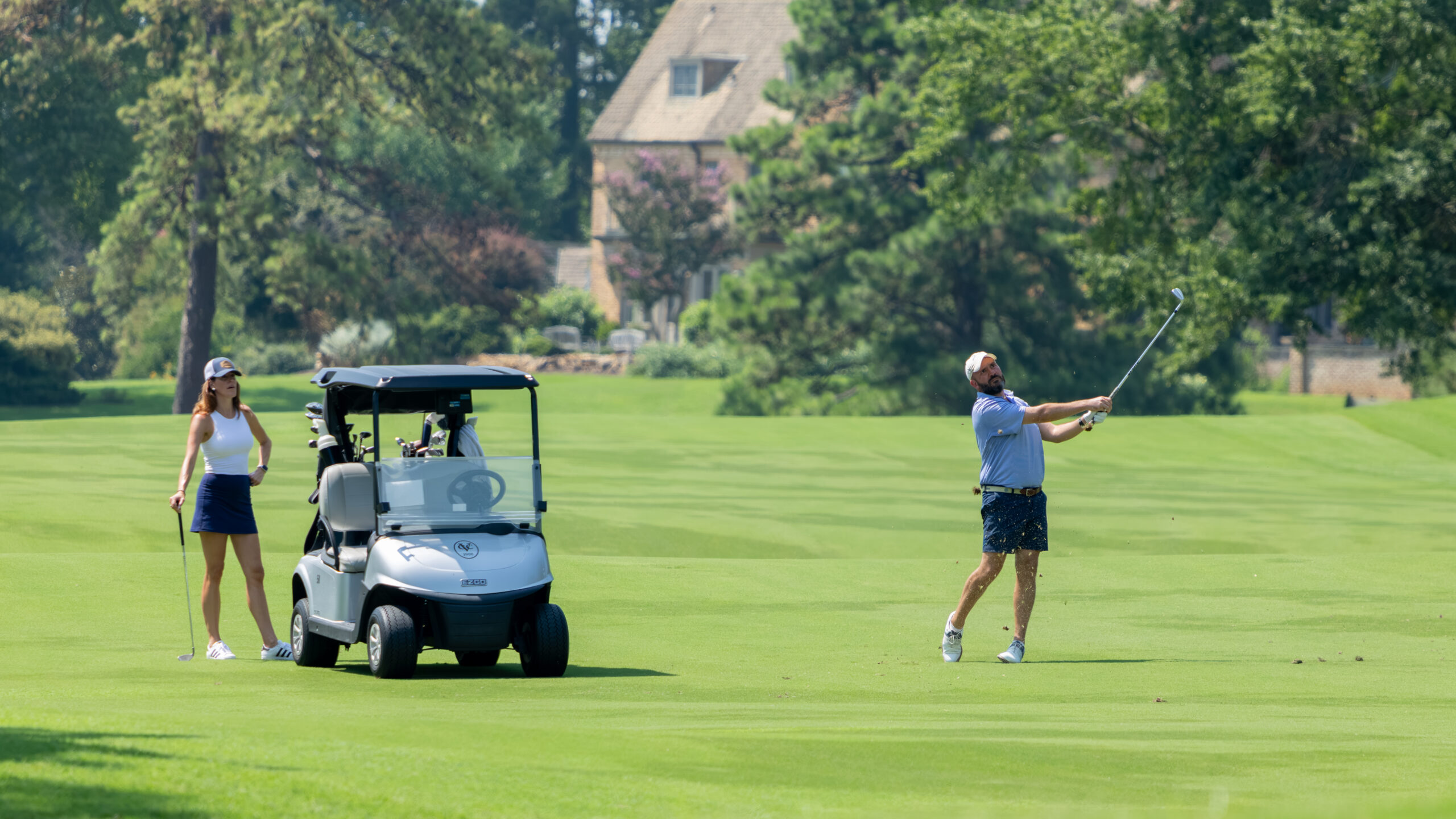 A man and woman golf on a green field with a white golf cart.