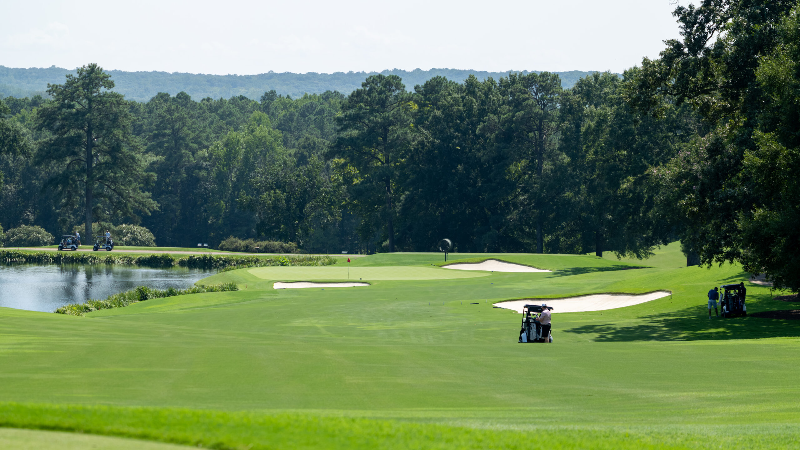 Golfers and carts on a green with bunkers and water features at Country Club of Virginia.