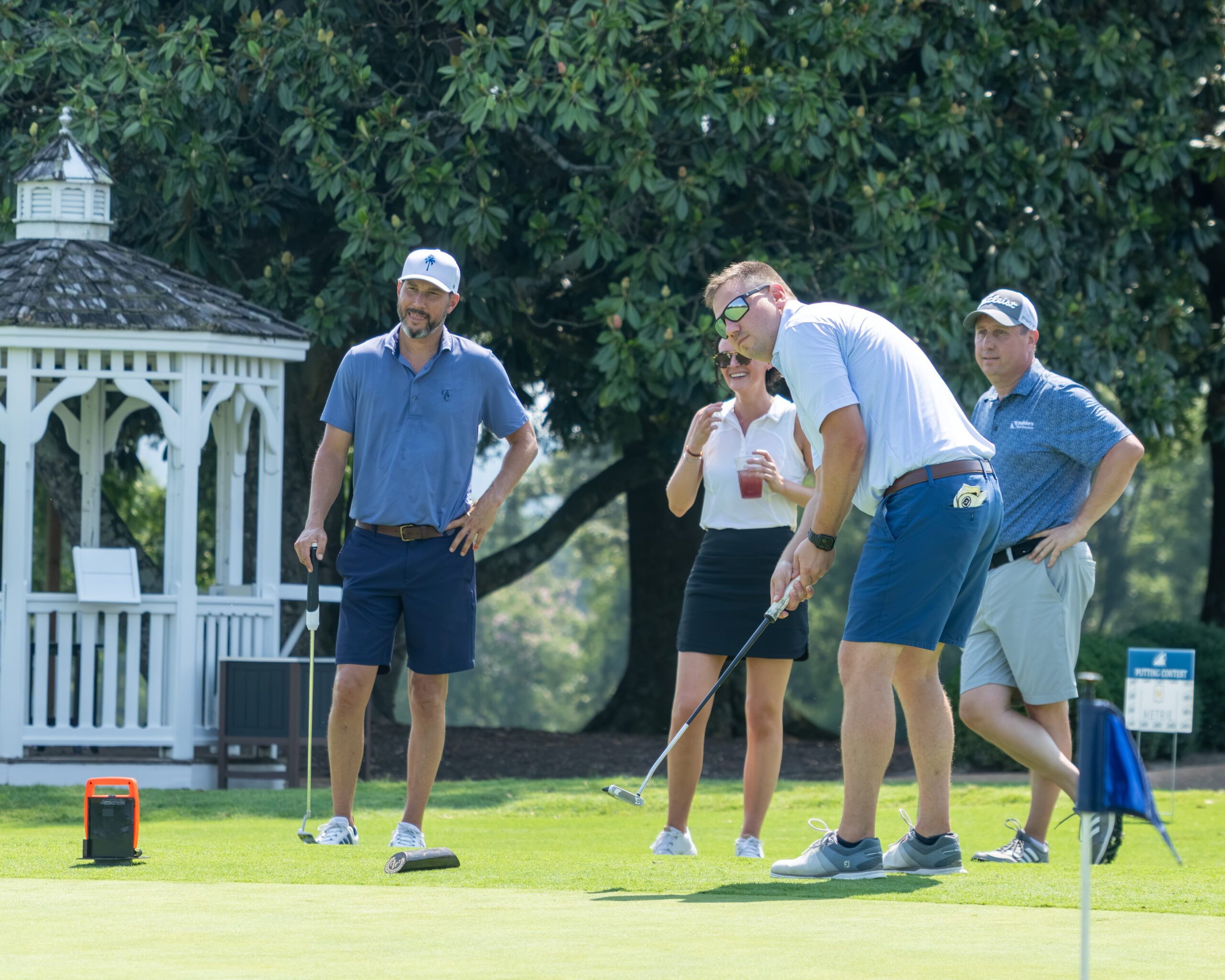 Four golfers on a green with a white gazebo in the background.