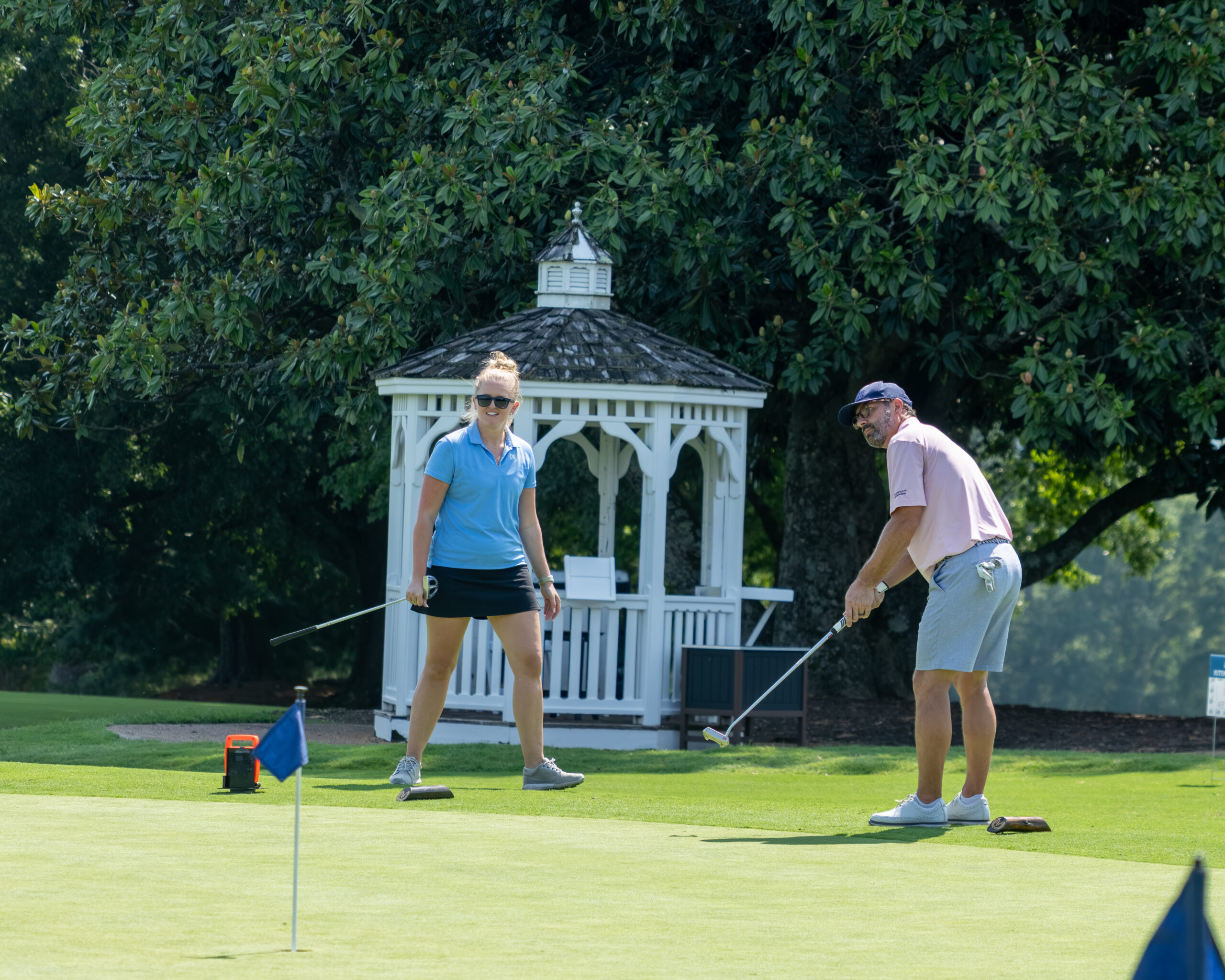 A man and woman golfers on a green near a white gazebo.