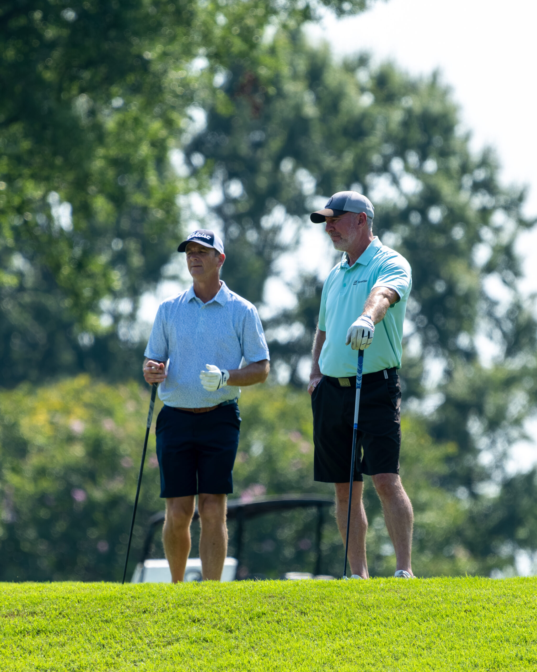 Two men in golf attire and hats are standing on a green at a golf course.