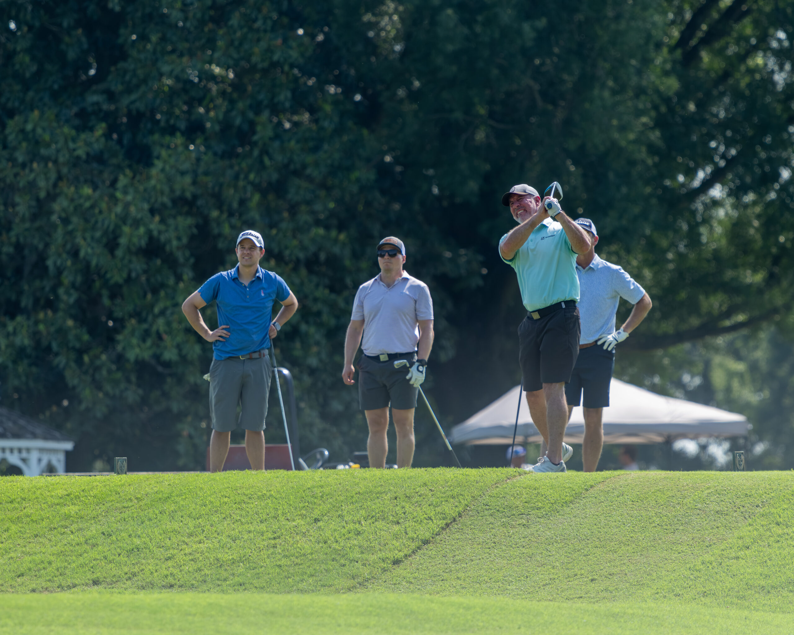 Four men golfers on a grass tee box with a golf club and ball.
