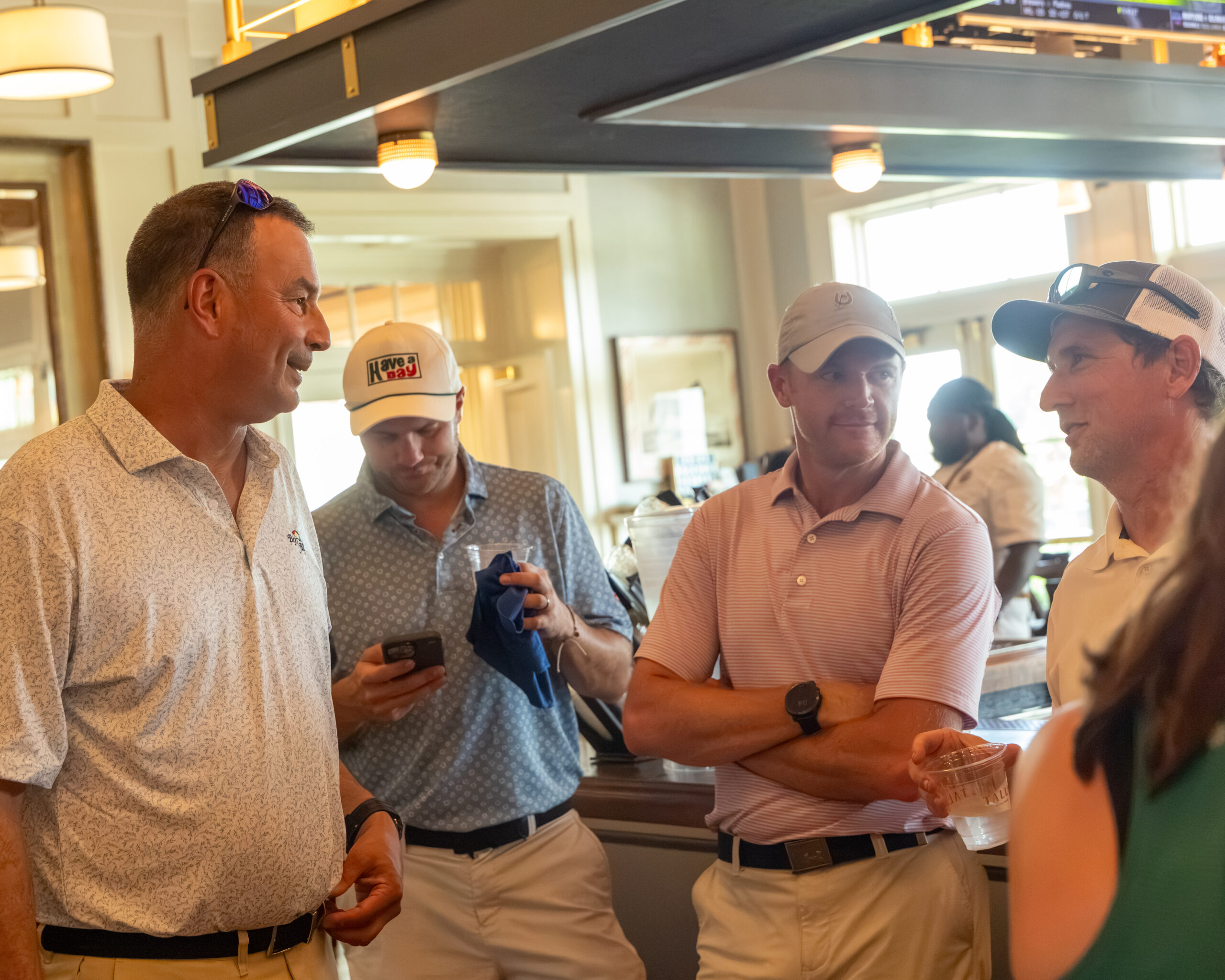 Four men are gathered around a bar area, talking and smiling.