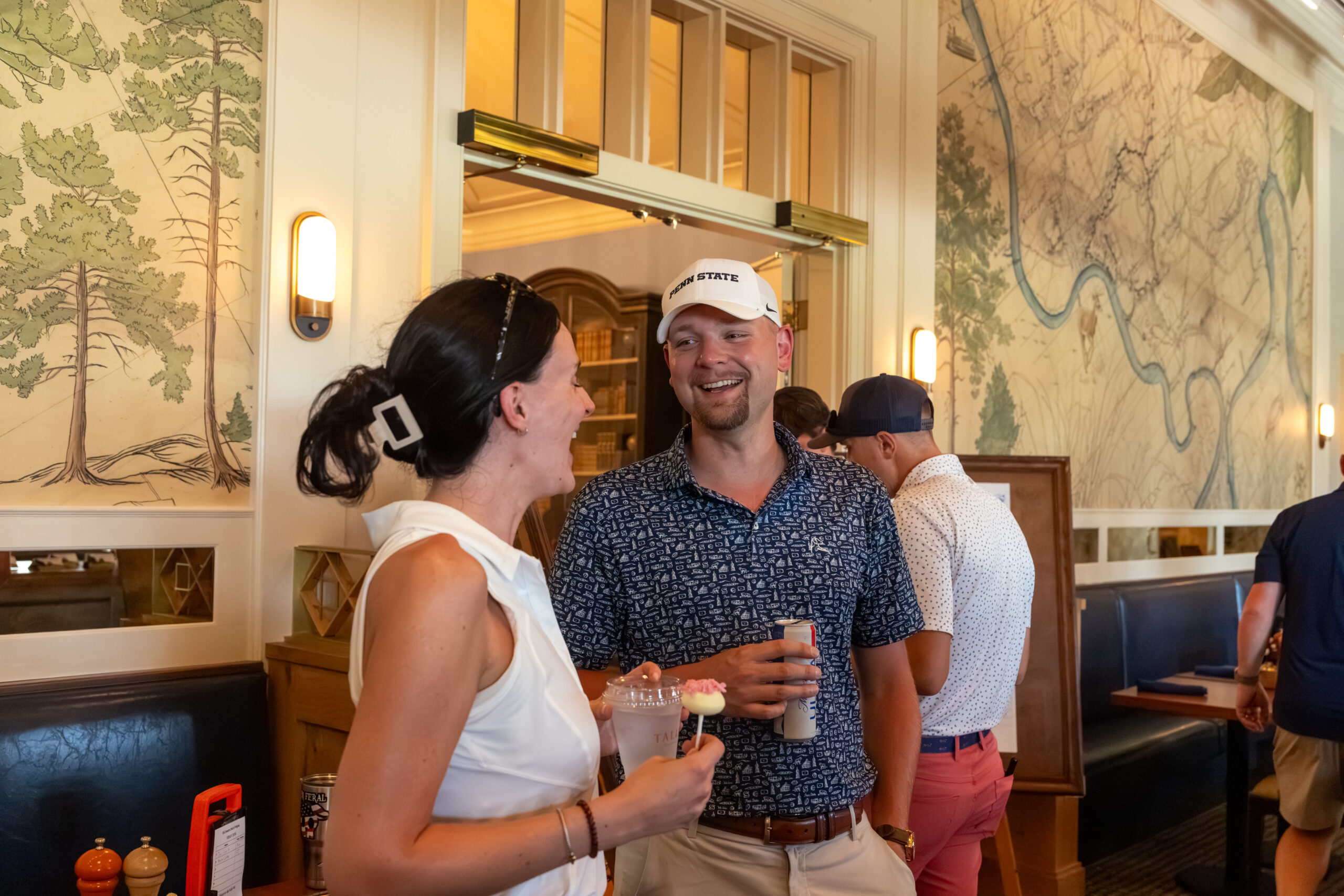 A man and a woman holding drinks and smiling at each other in a clubhouse setting.