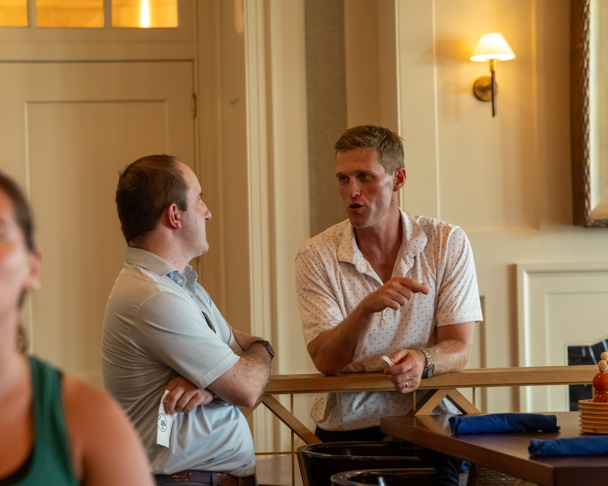 Two men are conversing and laughing while leaning against a wooden railing.