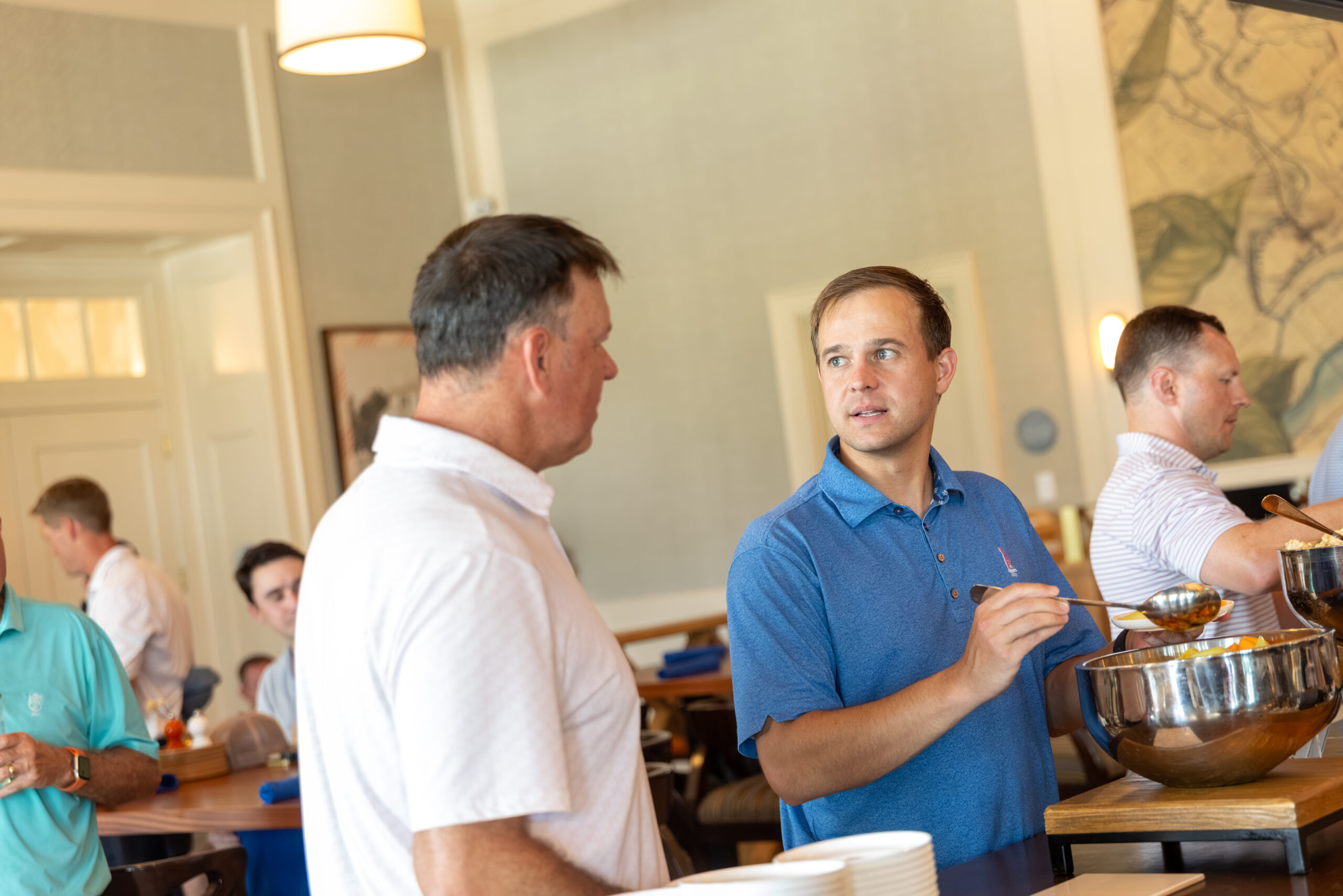 Two men conversing while one holds a small spoon near a large metal bowl.
