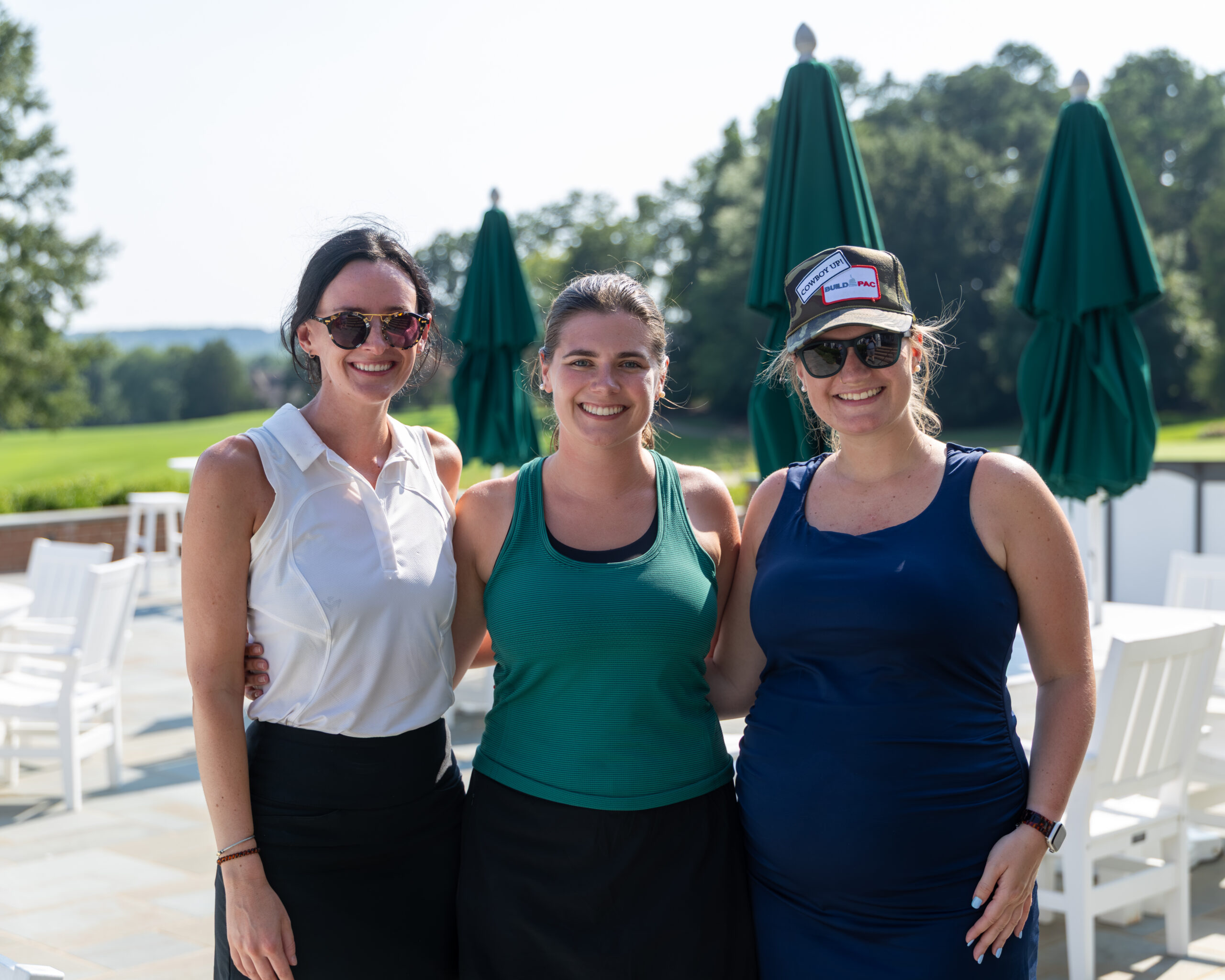 Three HBAV staff members smiling and posing for a photo outdoors near green umbrellas and white chairs.