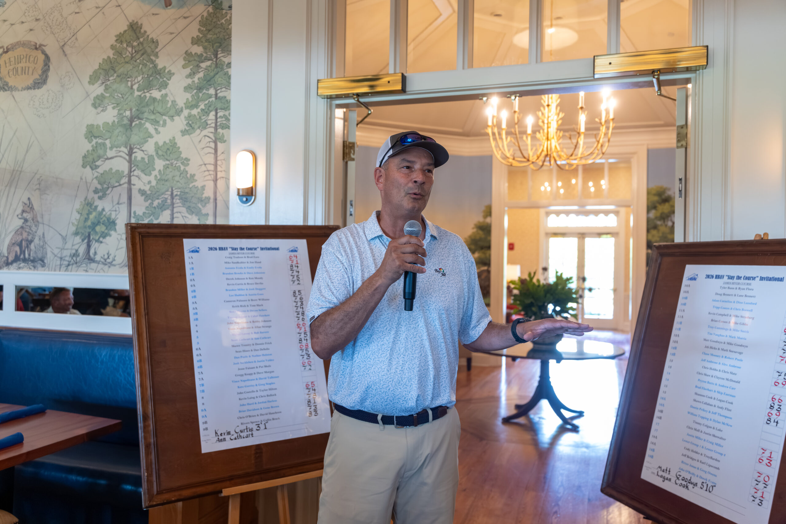 A man in a polo shirt and cap stands between two boards listing tournament rankings.