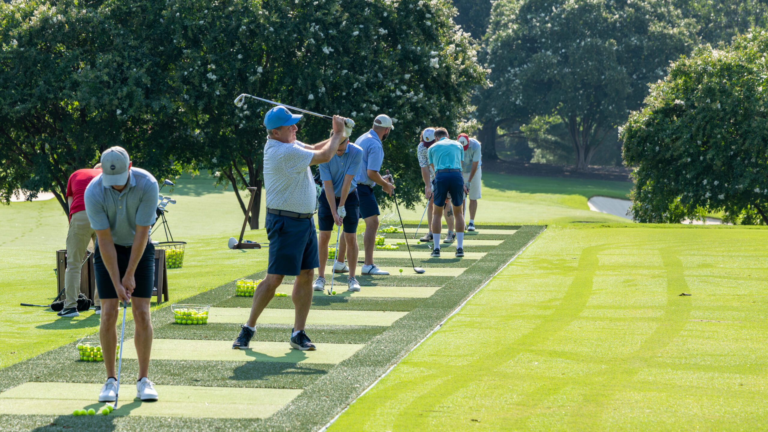A group of men practicing golf on an outdoor turf mat during a tournament.