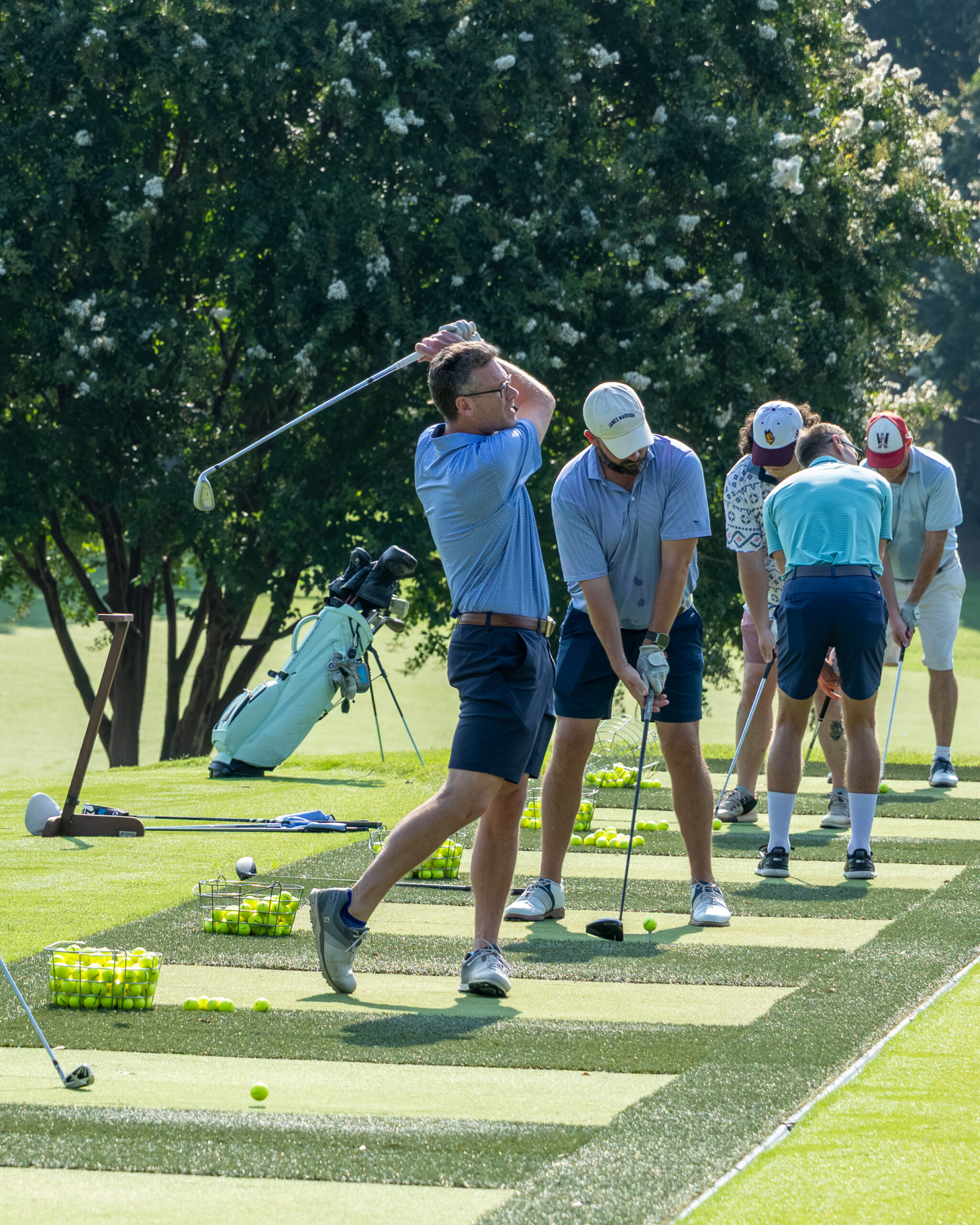 Four golfers practicing on a practice range with clubs and golf balls.
