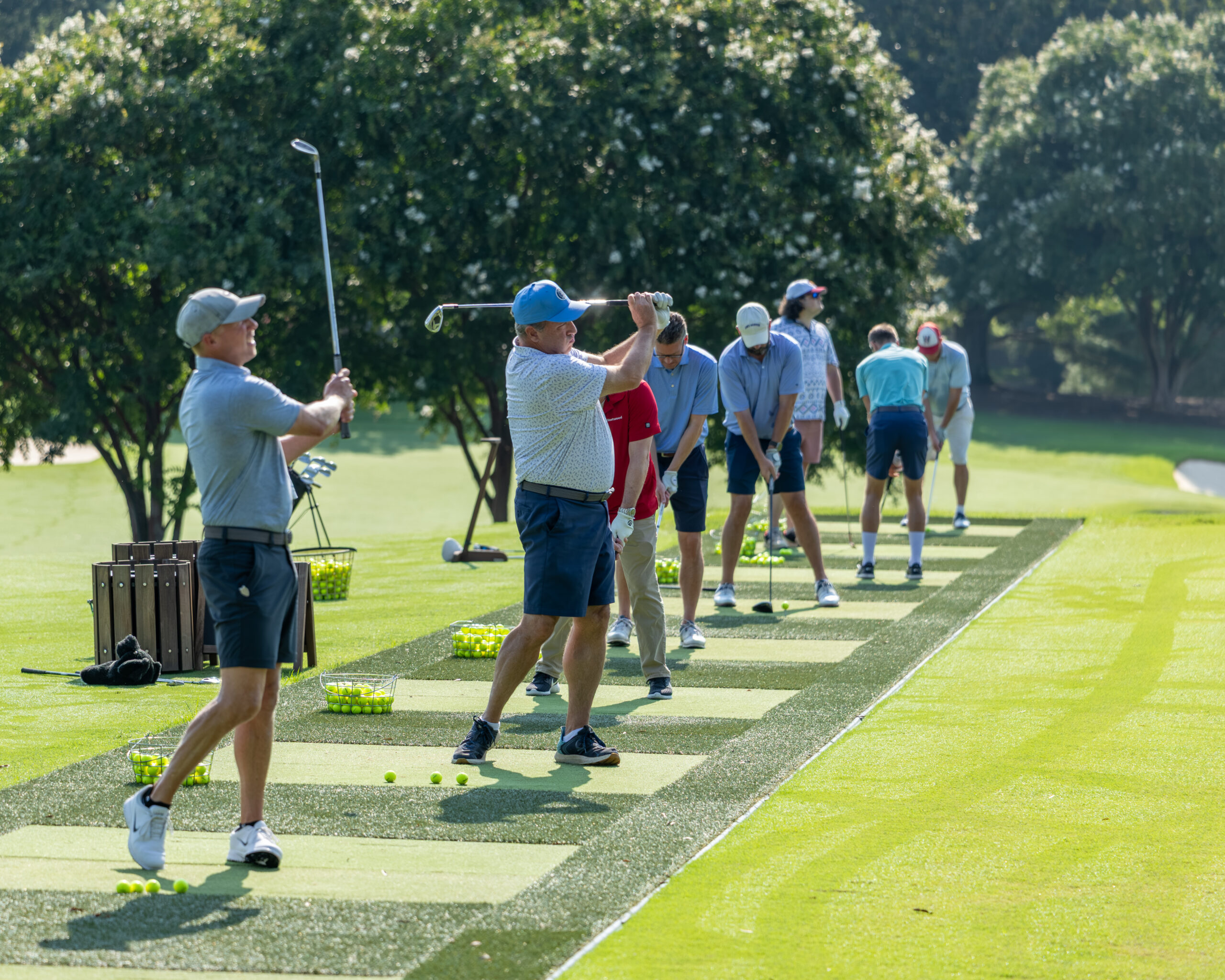 A line of golfers at a practice range preparing for their shots.