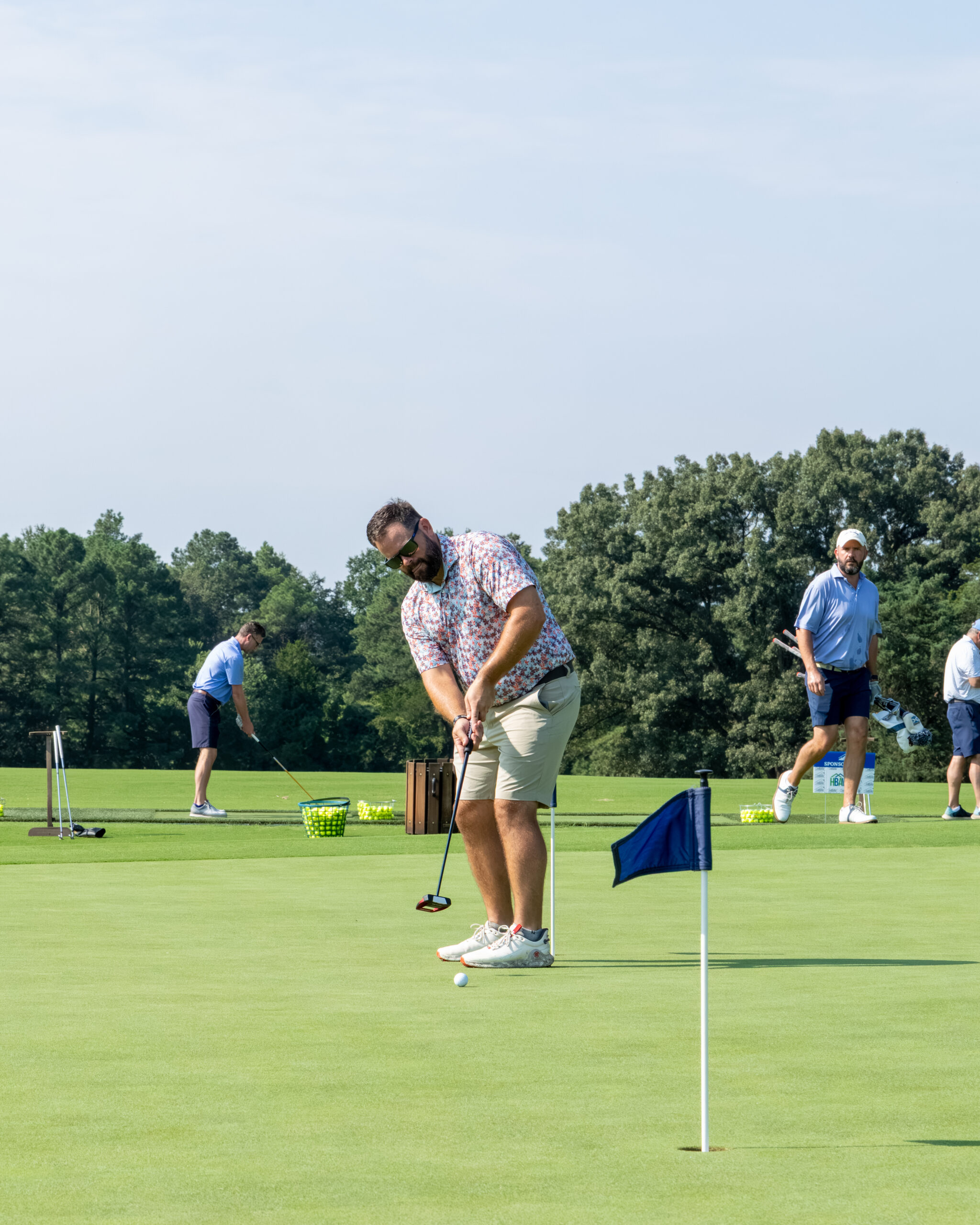 A man in a colorful patterned shirt and shorts stands over a golf ball on a green.