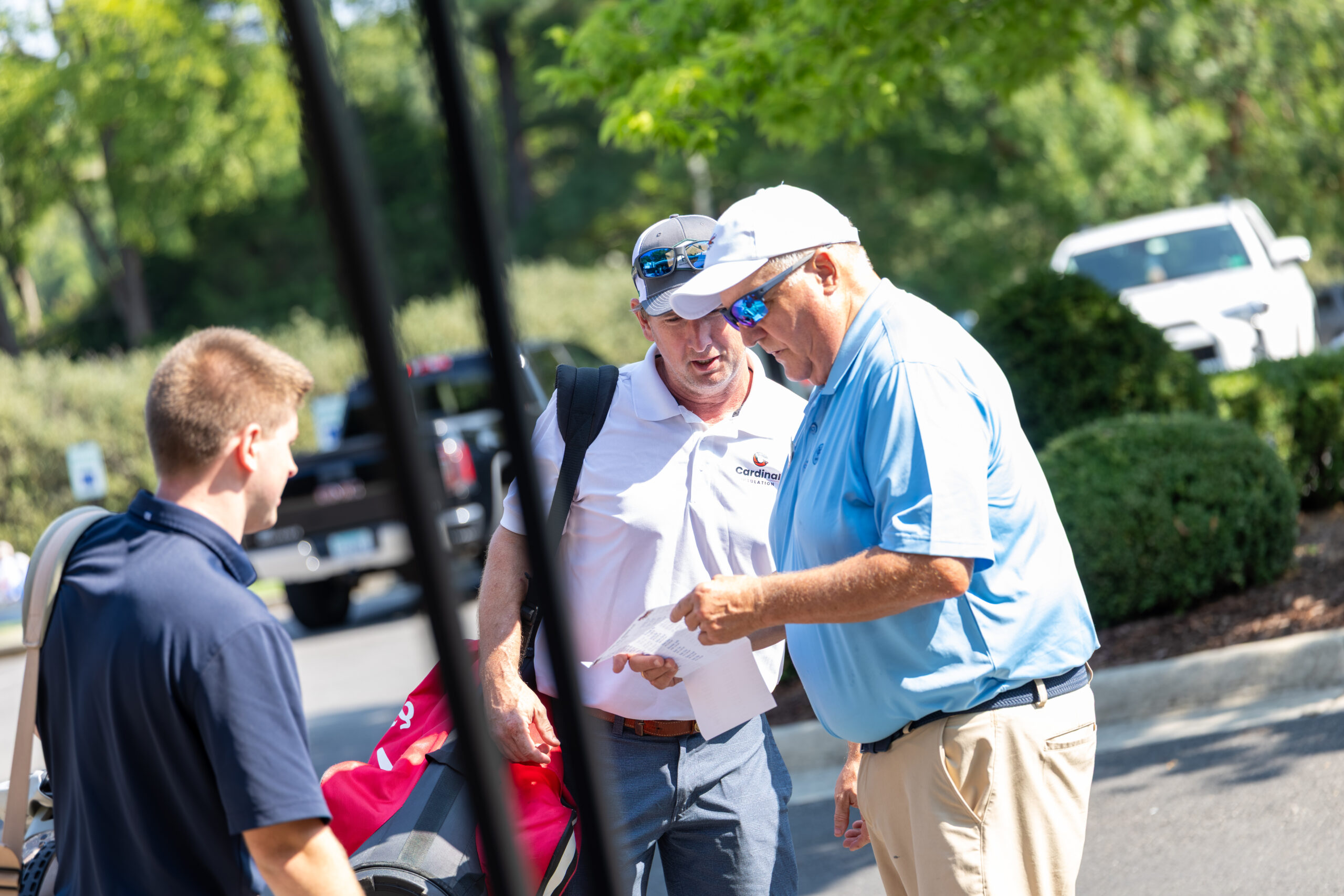 Two men at a golf course talking and looking at a paper while a third man watches.