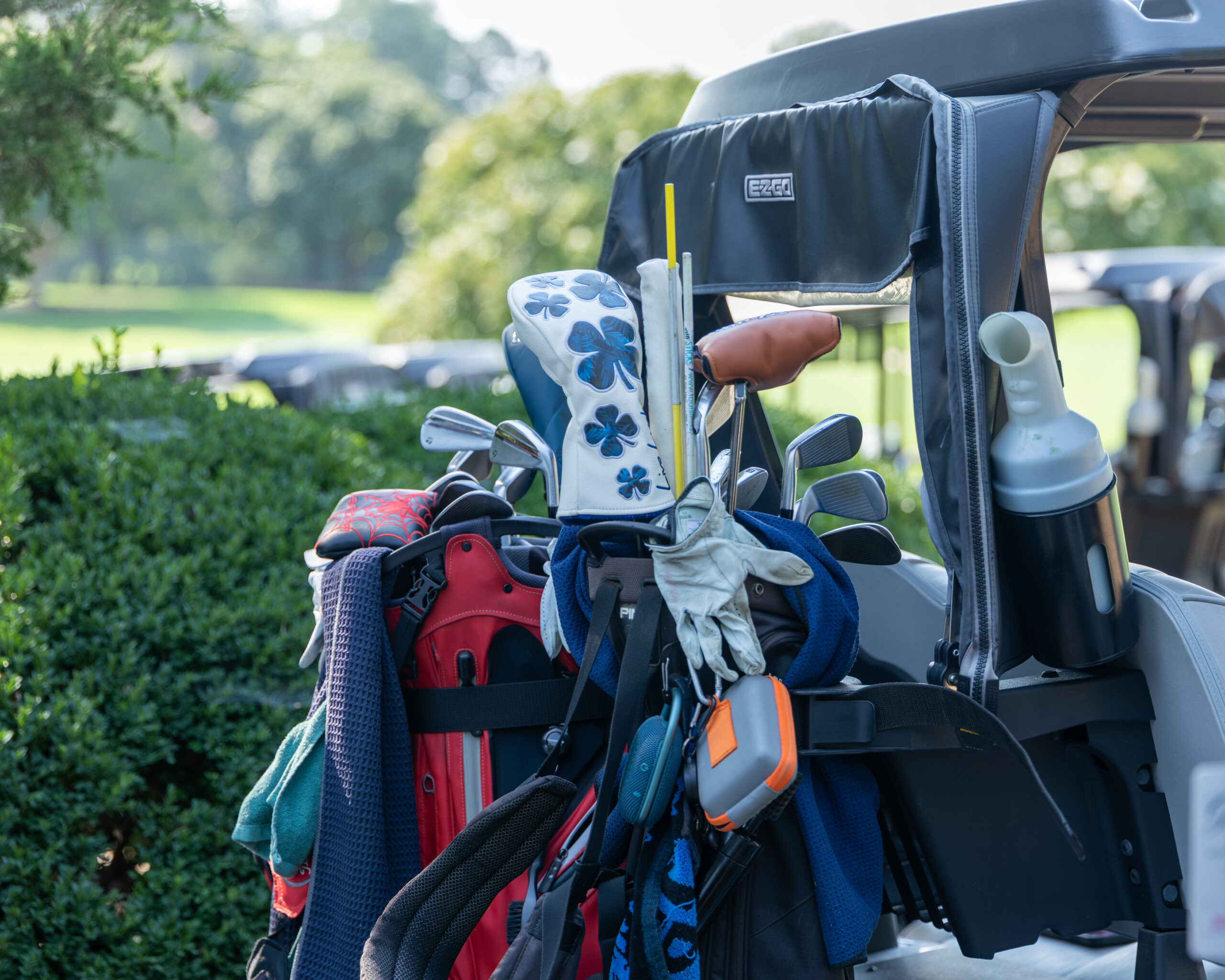 A golf bag and clubs are stashed on a golf cart in front of green grass and trees.