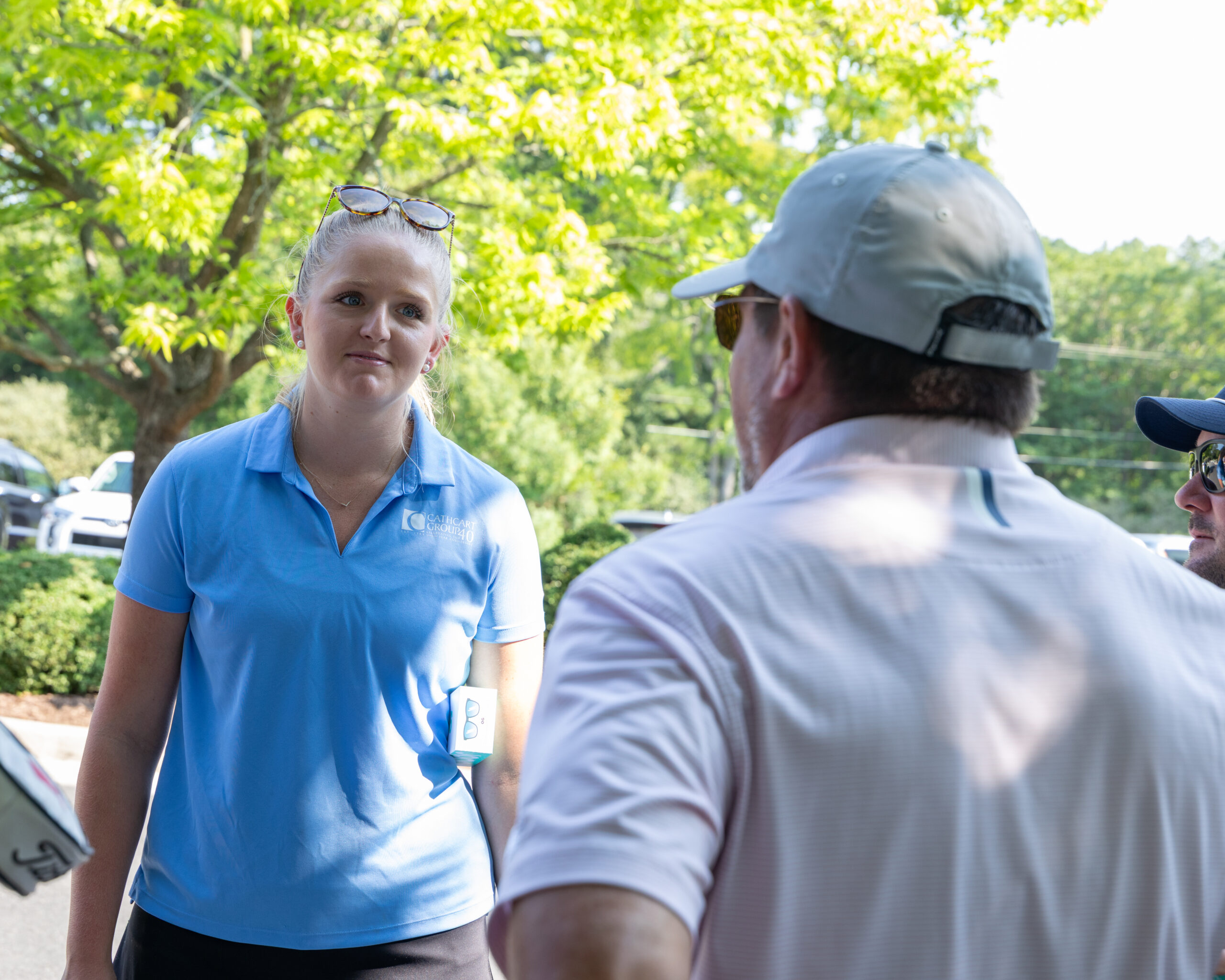 A woman in a blue polo shirt and a man in a white shirt and baseball cap are talking.