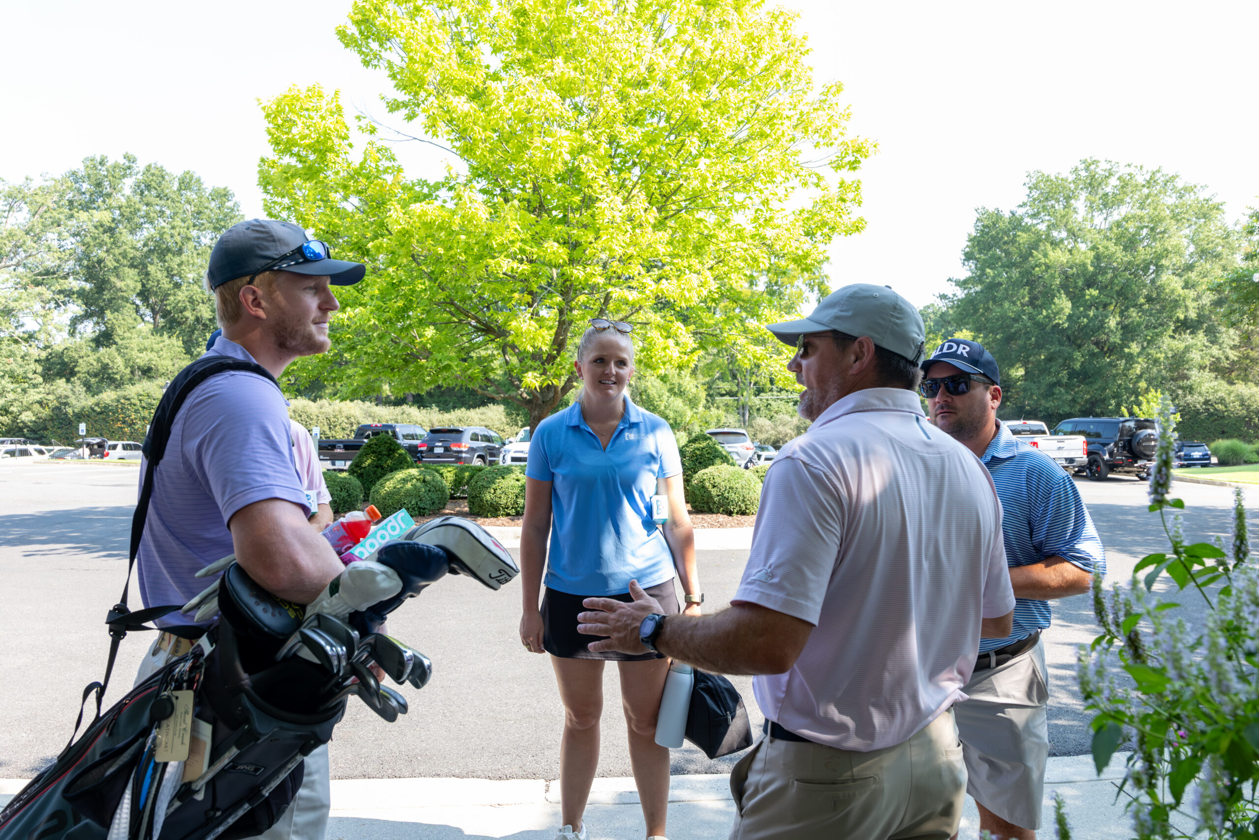 Four golfers standing on a paved path with green trees in background.
