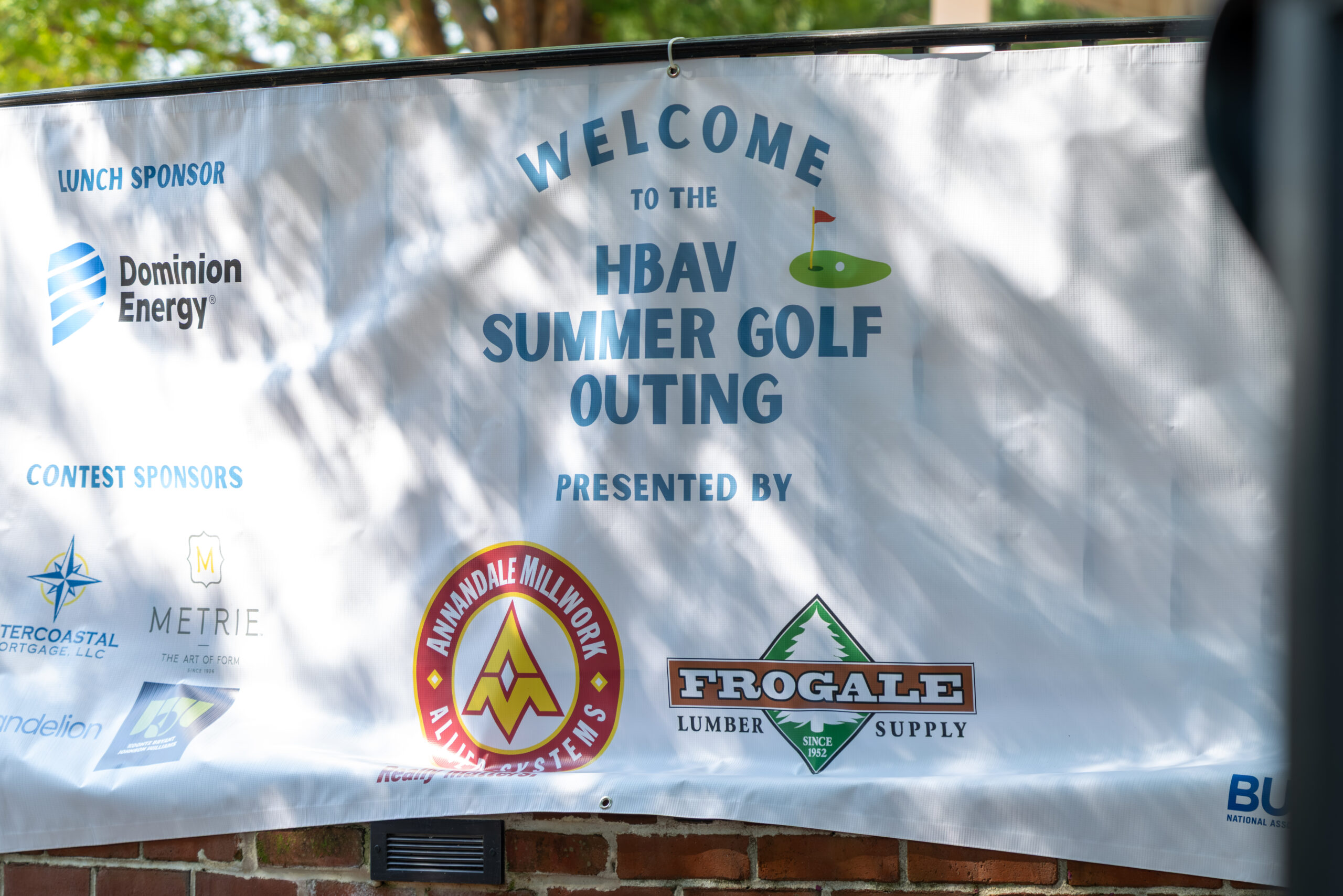 A banner hanging outdoors featuring text and logos for an HBAV Summer Golf Outing.