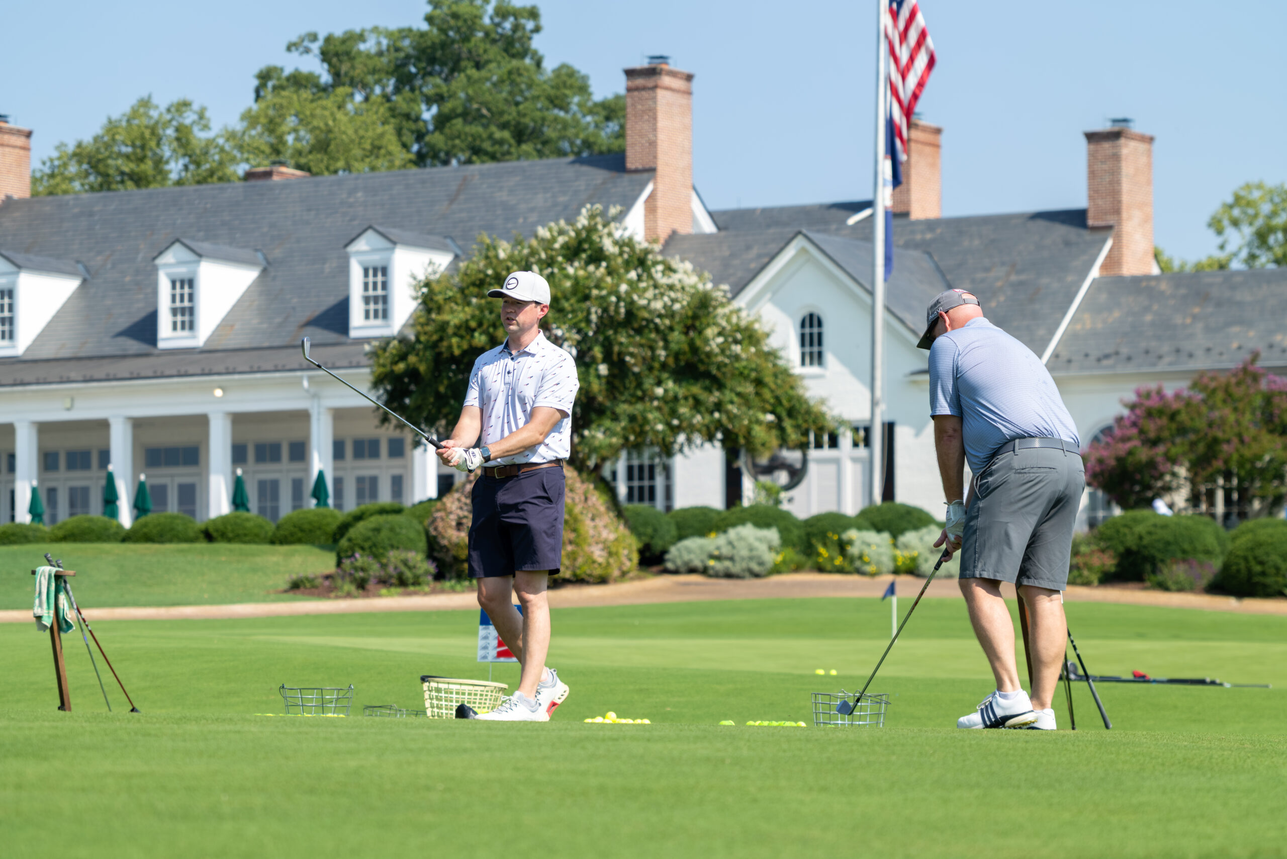 Two men on a golf course and holding golf clubs, practicing with balls.