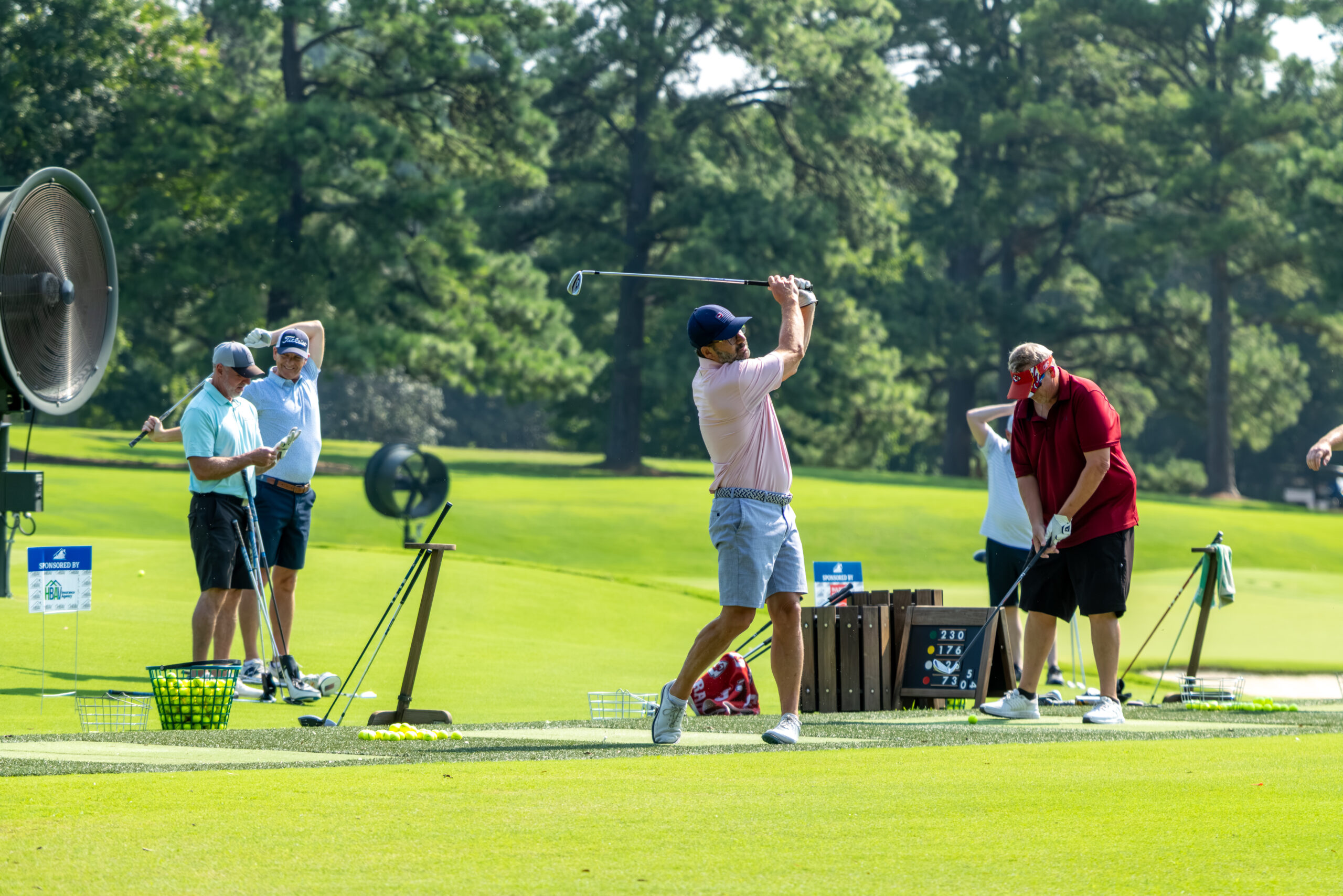 Three men playing golf on a grassy field with trees in the background.
