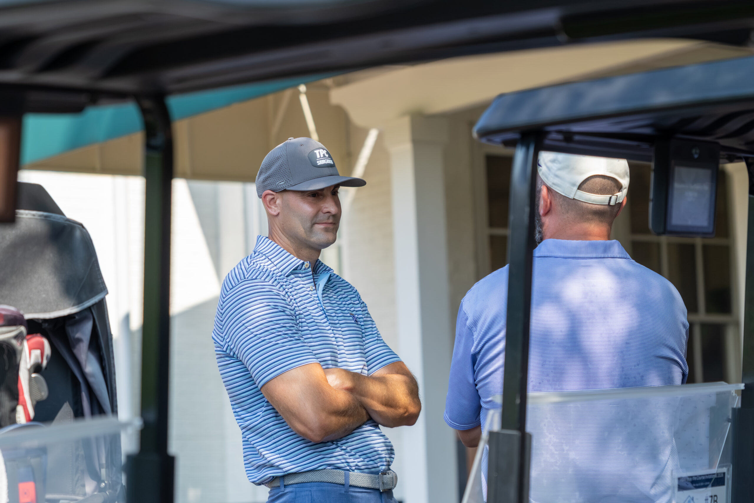 Two men in golf attire standing near golf carts on a sunny day.
