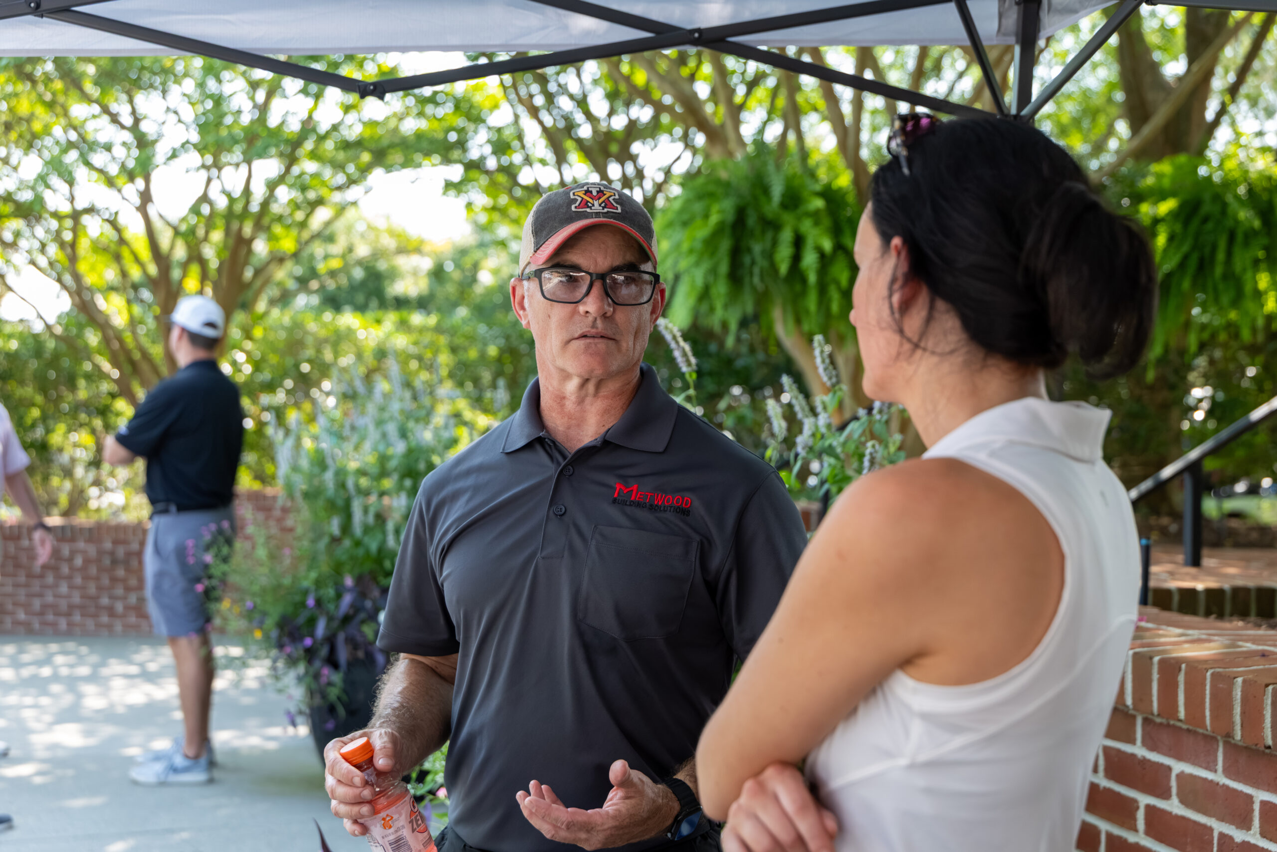 A man and a woman are talking under a white canopy tent while others are seen in the background.