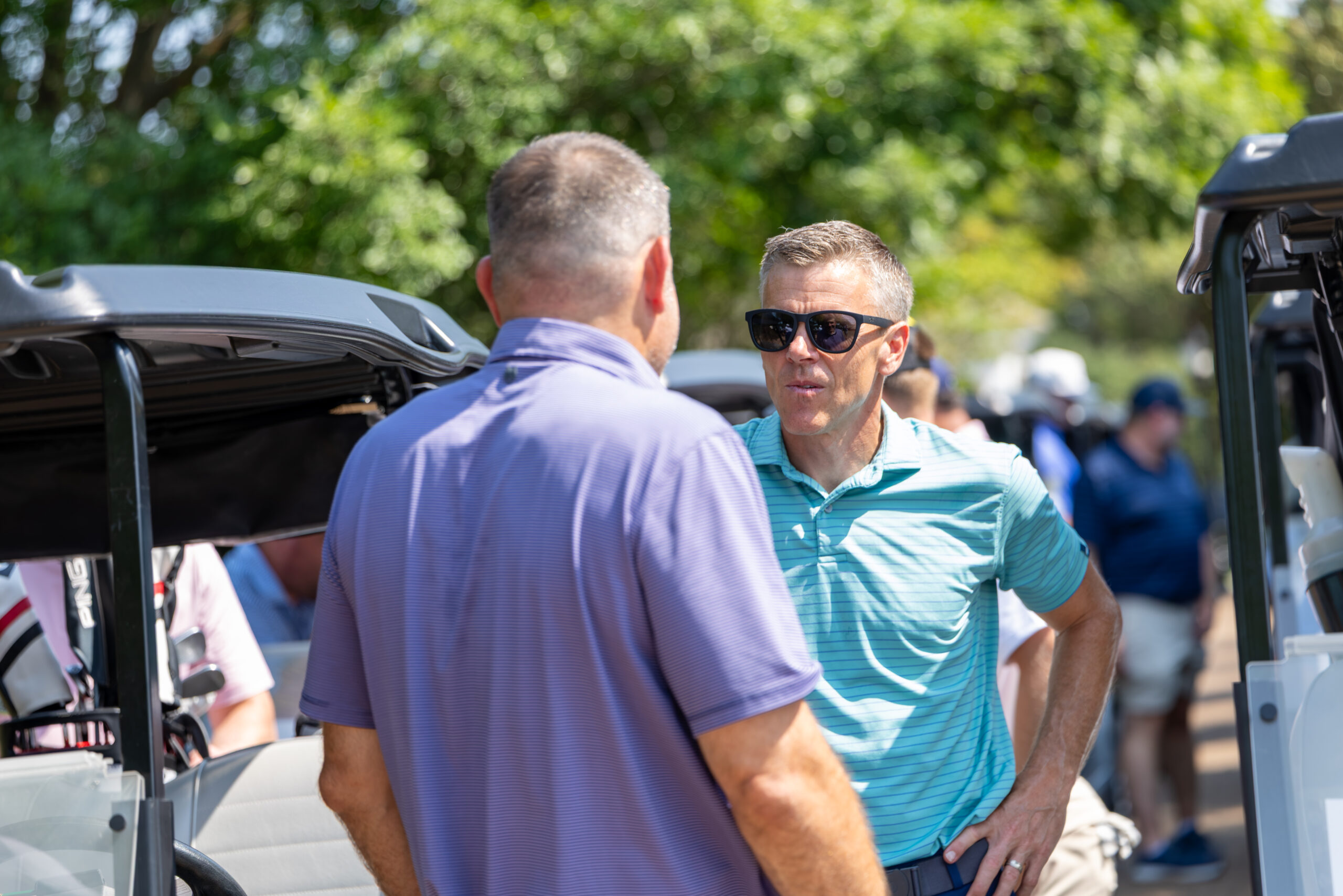 Two men talking near a golf cart on a grass-covered field.