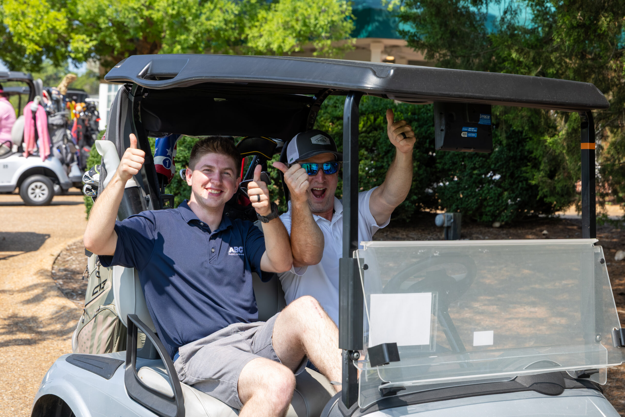 Two men in a golf cart giving thumbs up and smiling.