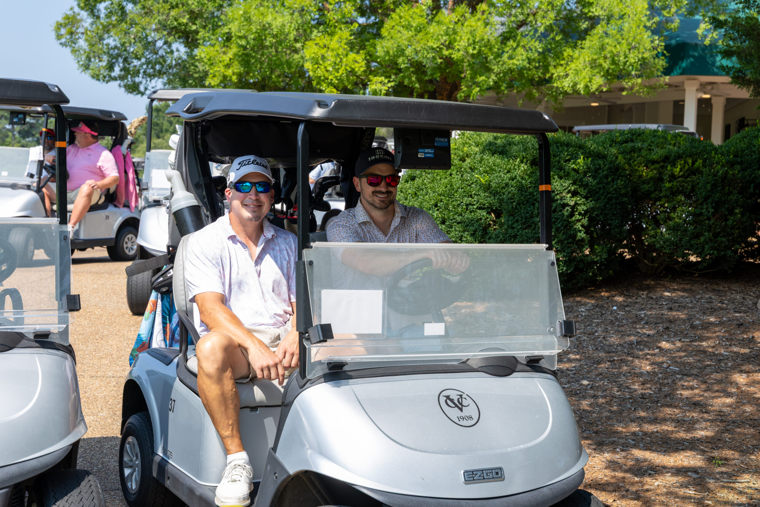 Two men sitting in a golf cart at a golf course.