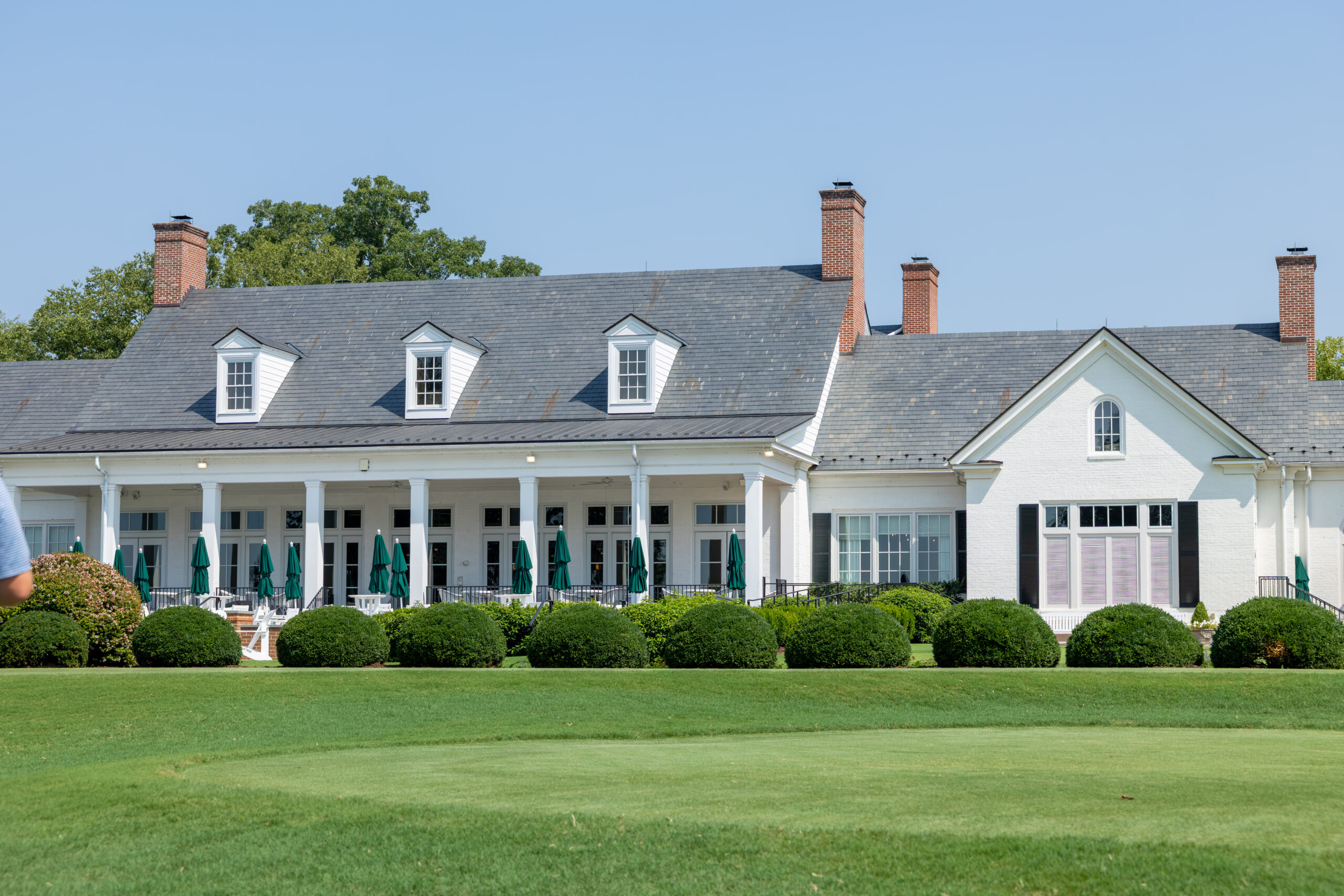 The James River Course clubhouse building with many windows and a front porch with green umbrellas.