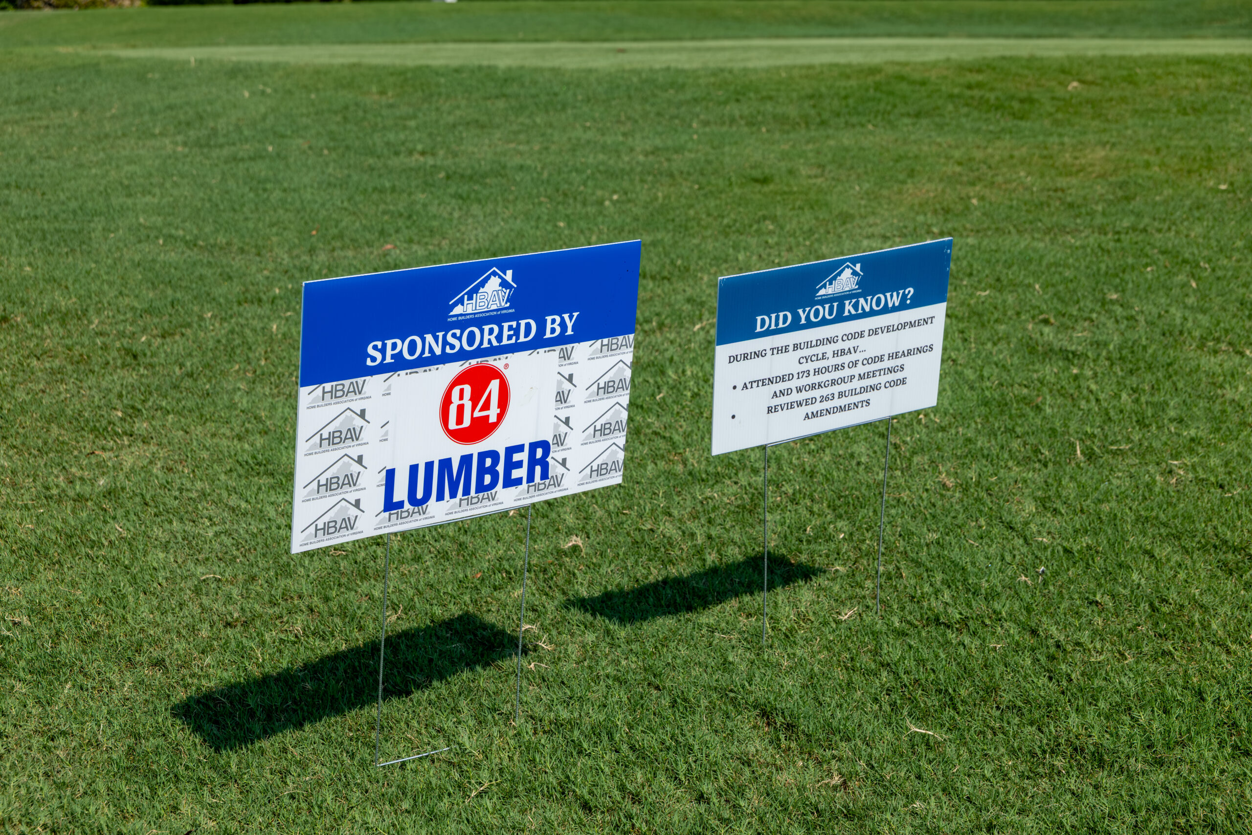 Two signs on a golf course: one says 'SPONSORED BY 84 LUMBER', and another asks 'DID YOU KNOW?' about items HBAV has fought using BuildPAC funding.