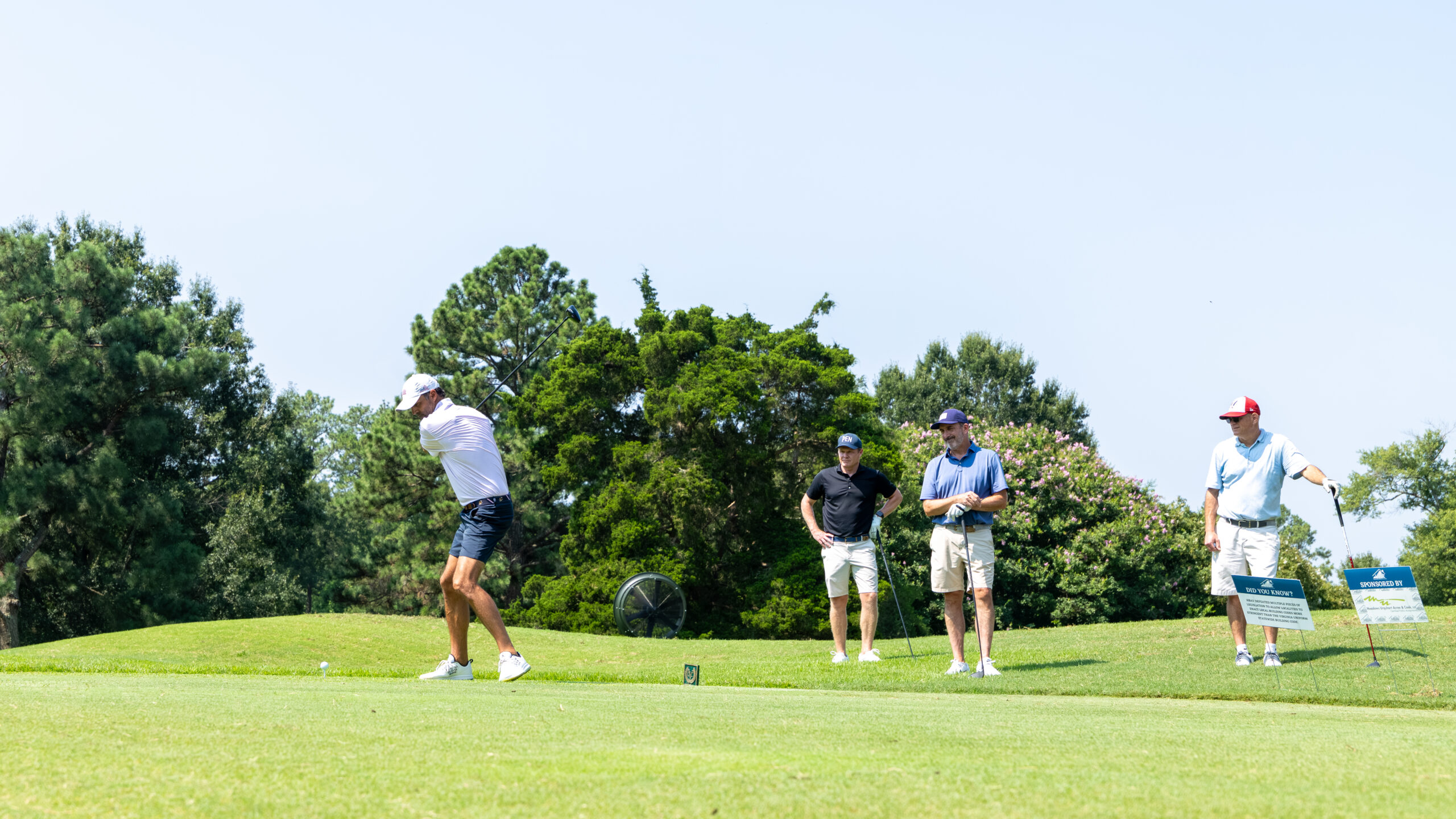 Four golfers with golf clubs on a green under clear skies.