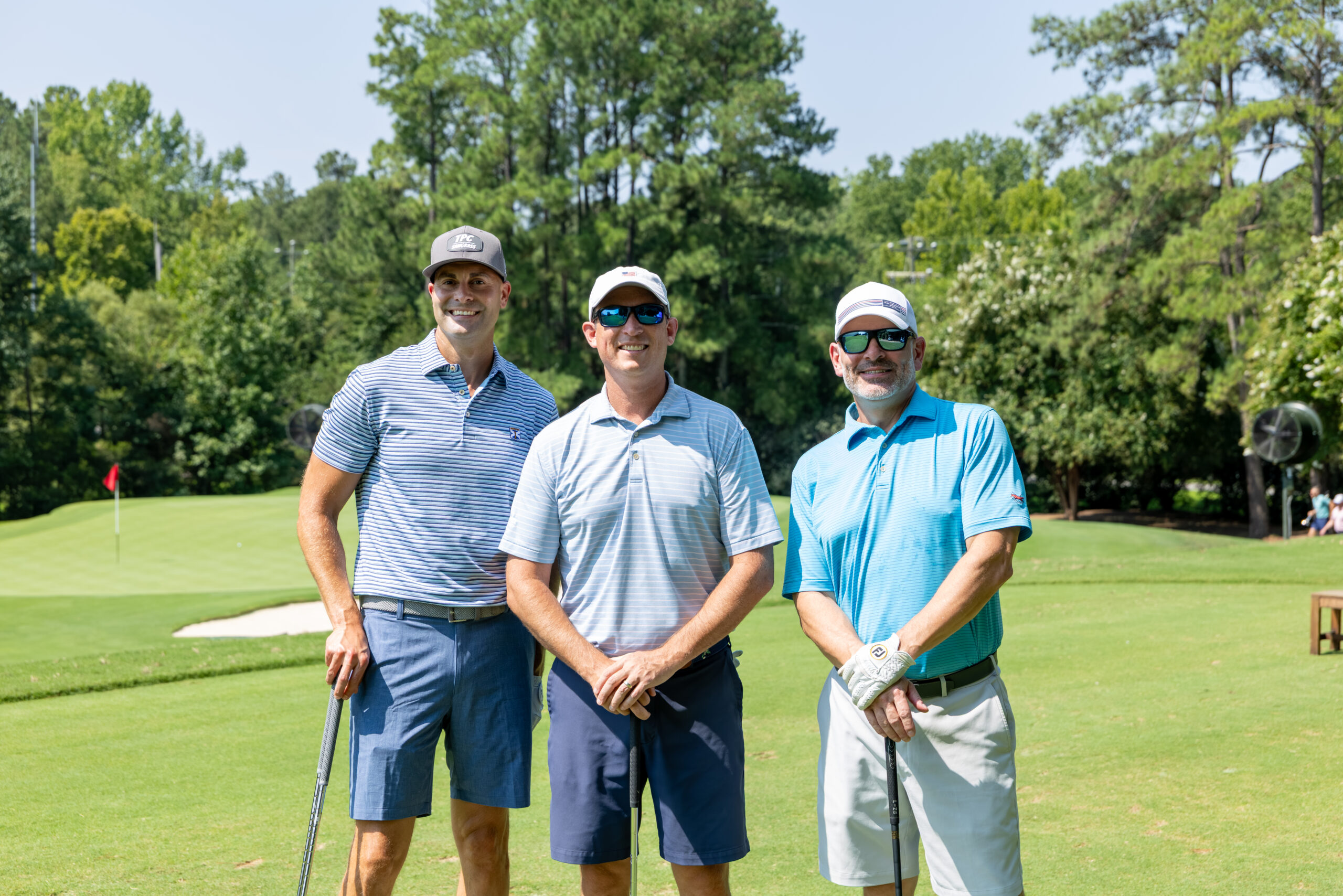 Three men wearing golf attire and hats standing on a golf course.