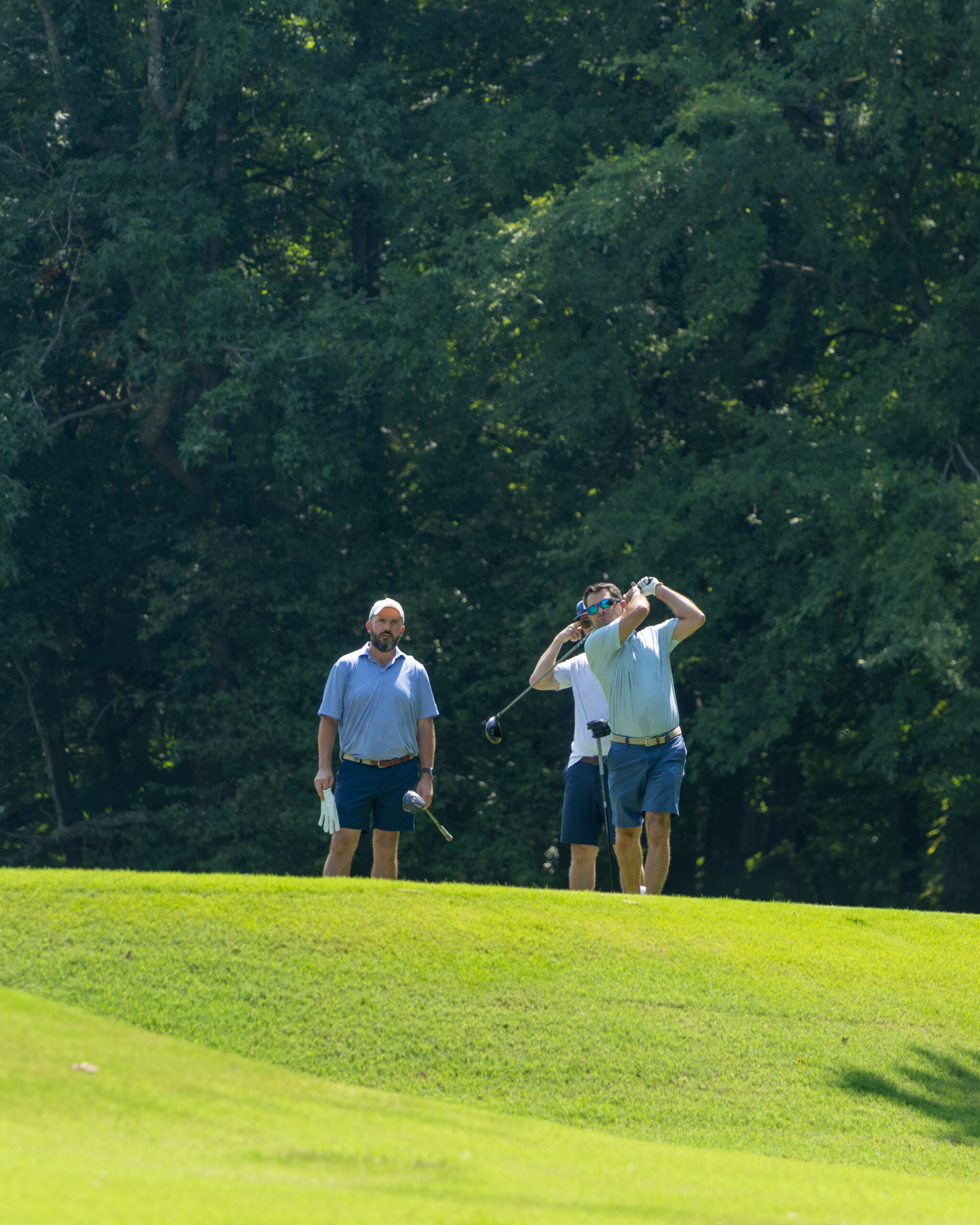 Two men on a golf course with one man swinging a golf club.