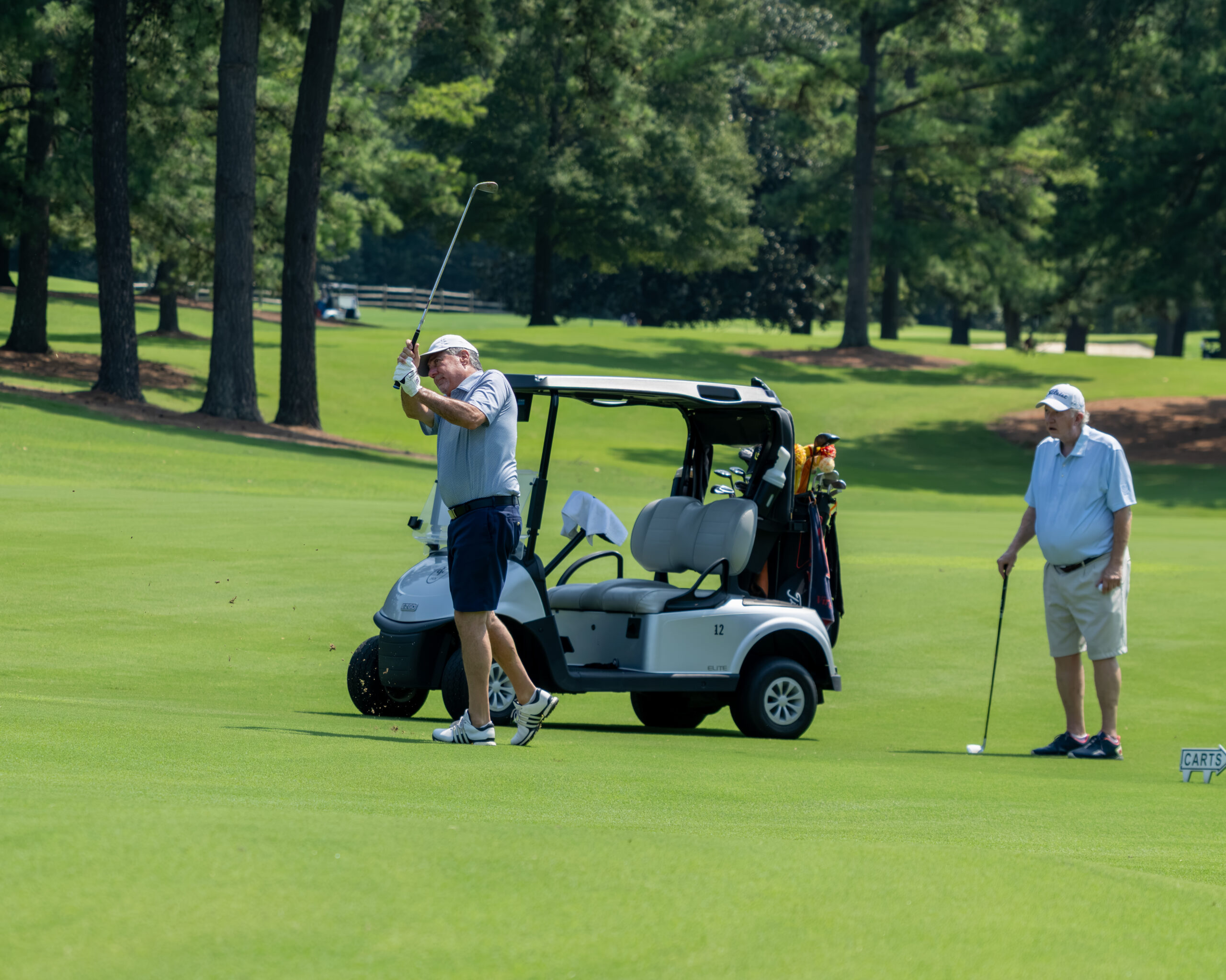 Two men golfing on a lush green fairway near a golf cart.